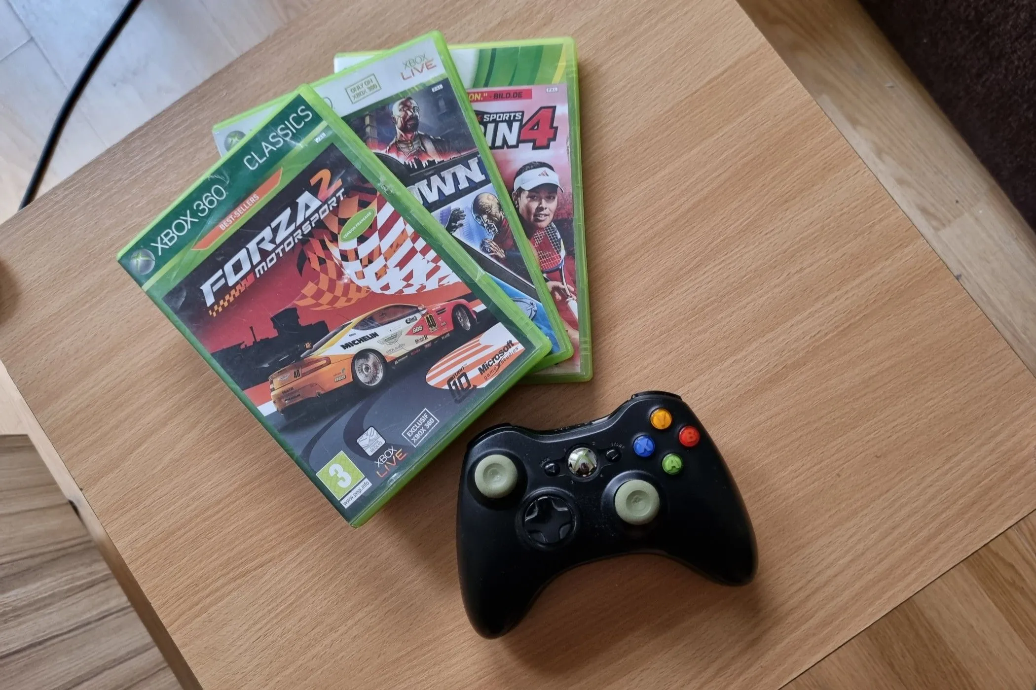 Bộ sưu tập đĩa game Xbox 360 cùng tay cầm điều khiển trên bàn, minh họa kho tàng trò chơi phong phú và giá cả phải chăng.
