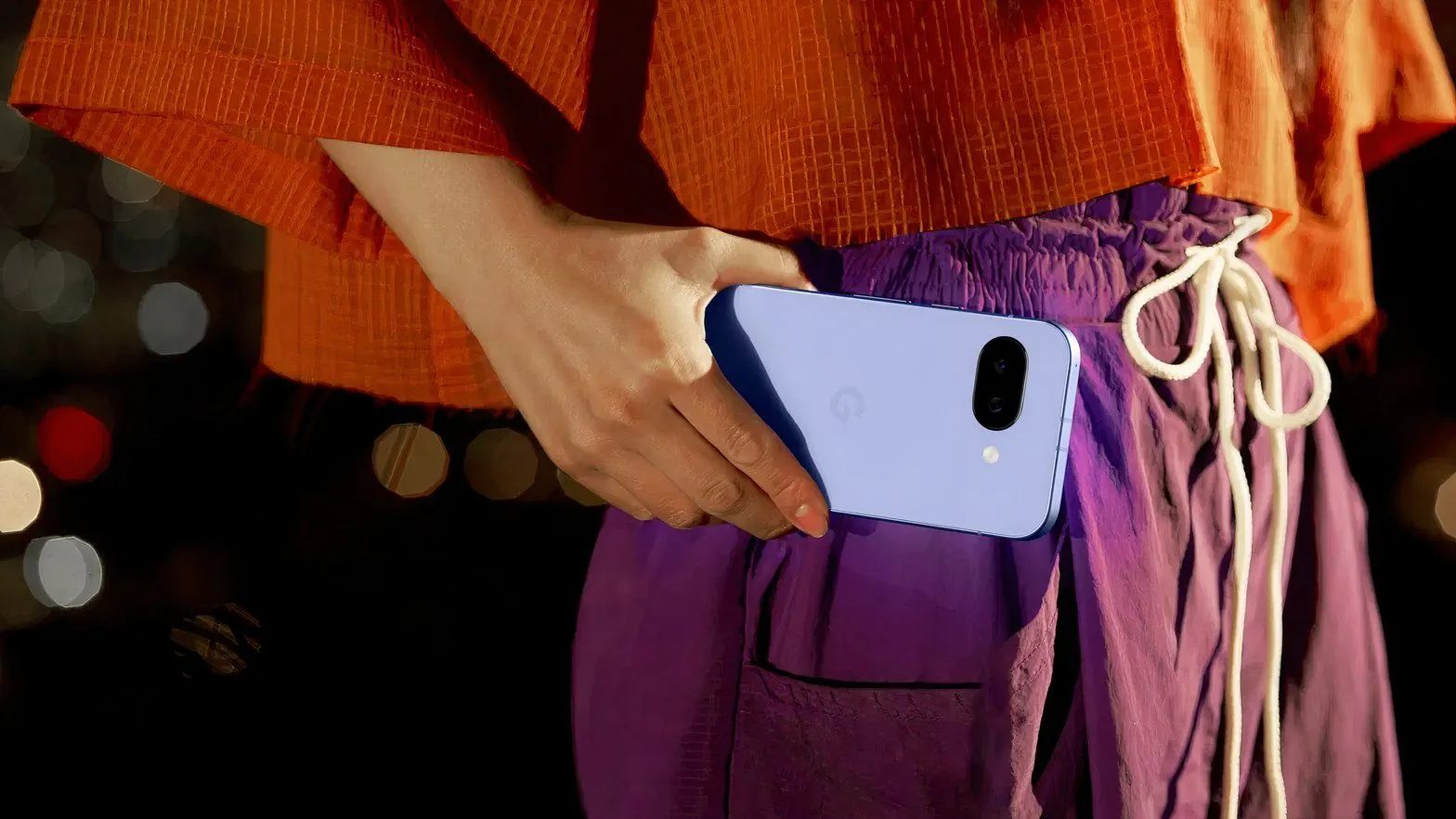 Cận cảnh một người phụ nữ cầm điện thoại Google Pixel 9a ở tầm ngang eo, thể hiện thiết kế cụm camera ấn tượng.