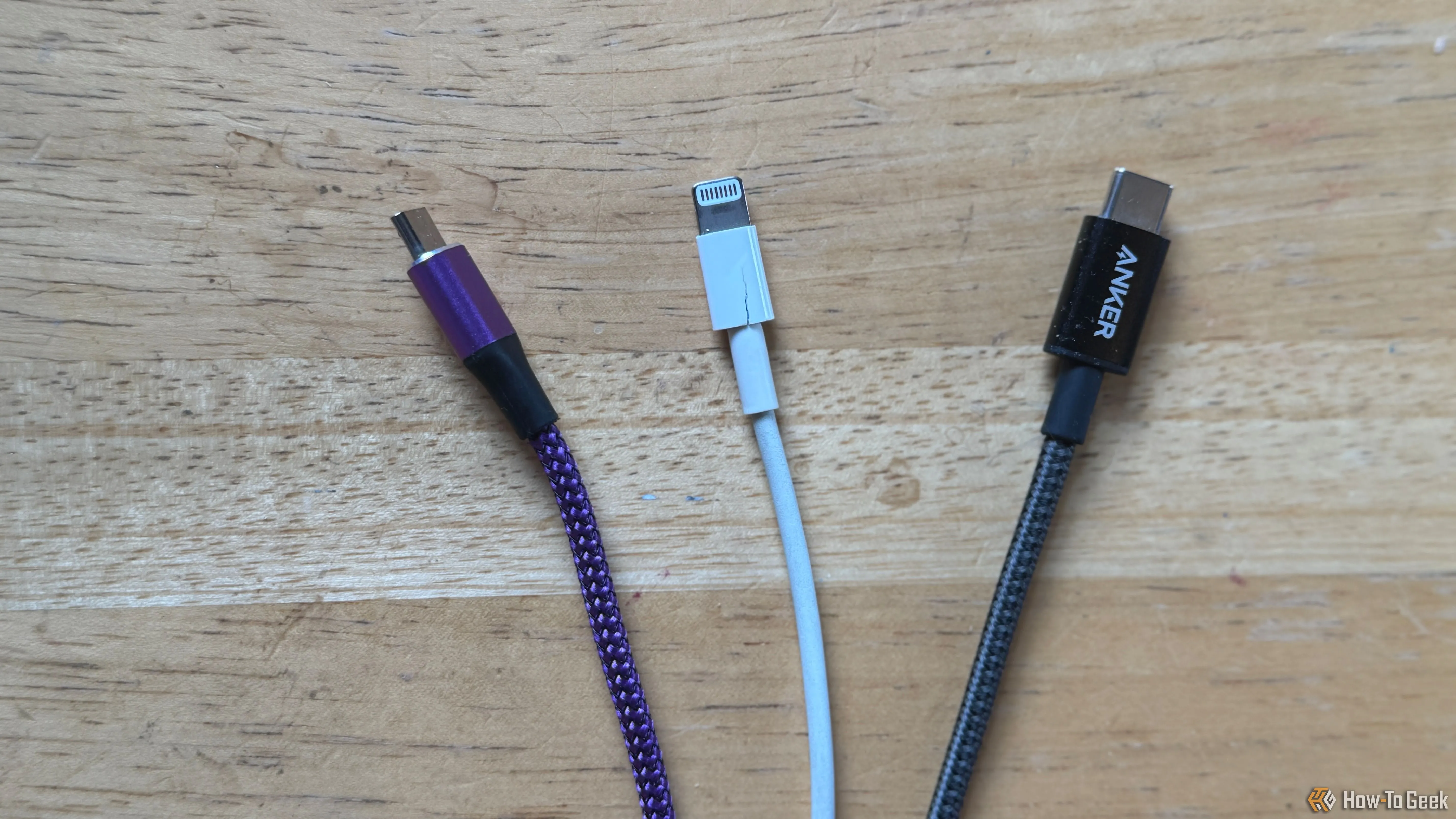 Cáp sạc Micro-USB màu tím, Lightning màu trắng và USB-C màu xám đặt trên bàn, minh họa cách phân biệt dây sạc dễ dàng bằng màu sắc