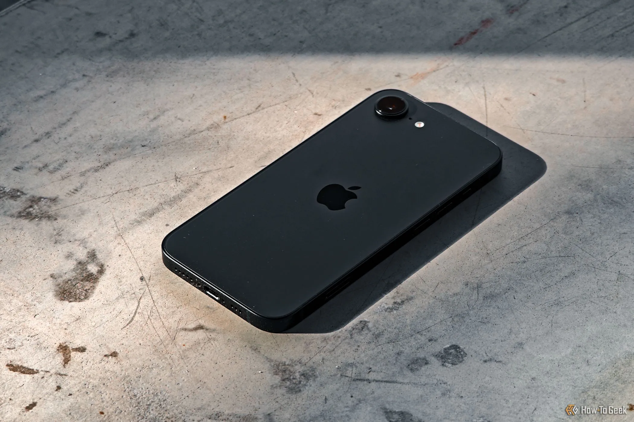 Điện thoại iPhone 16e úp mặt xuống nền bê tông, thể hiện độ bền và chip A18 mạnh mẽ.