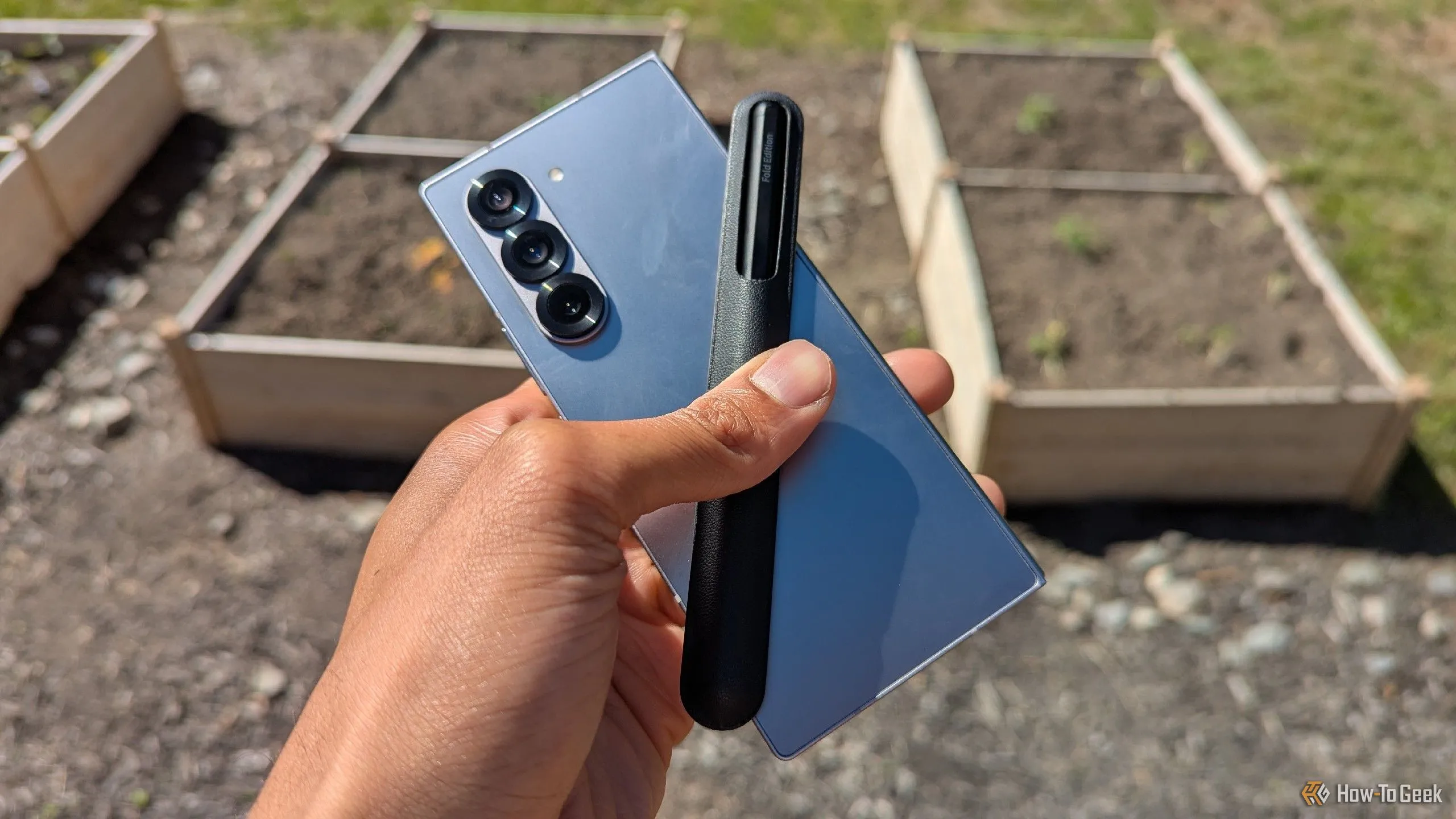 Điện thoại Samsung Galaxy Z Fold 6 màu xanh mint cùng bút S Pen đặt trước vườn cây, thể hiện vẻ đẹp nguyên bản và độ bền của thiết bị.