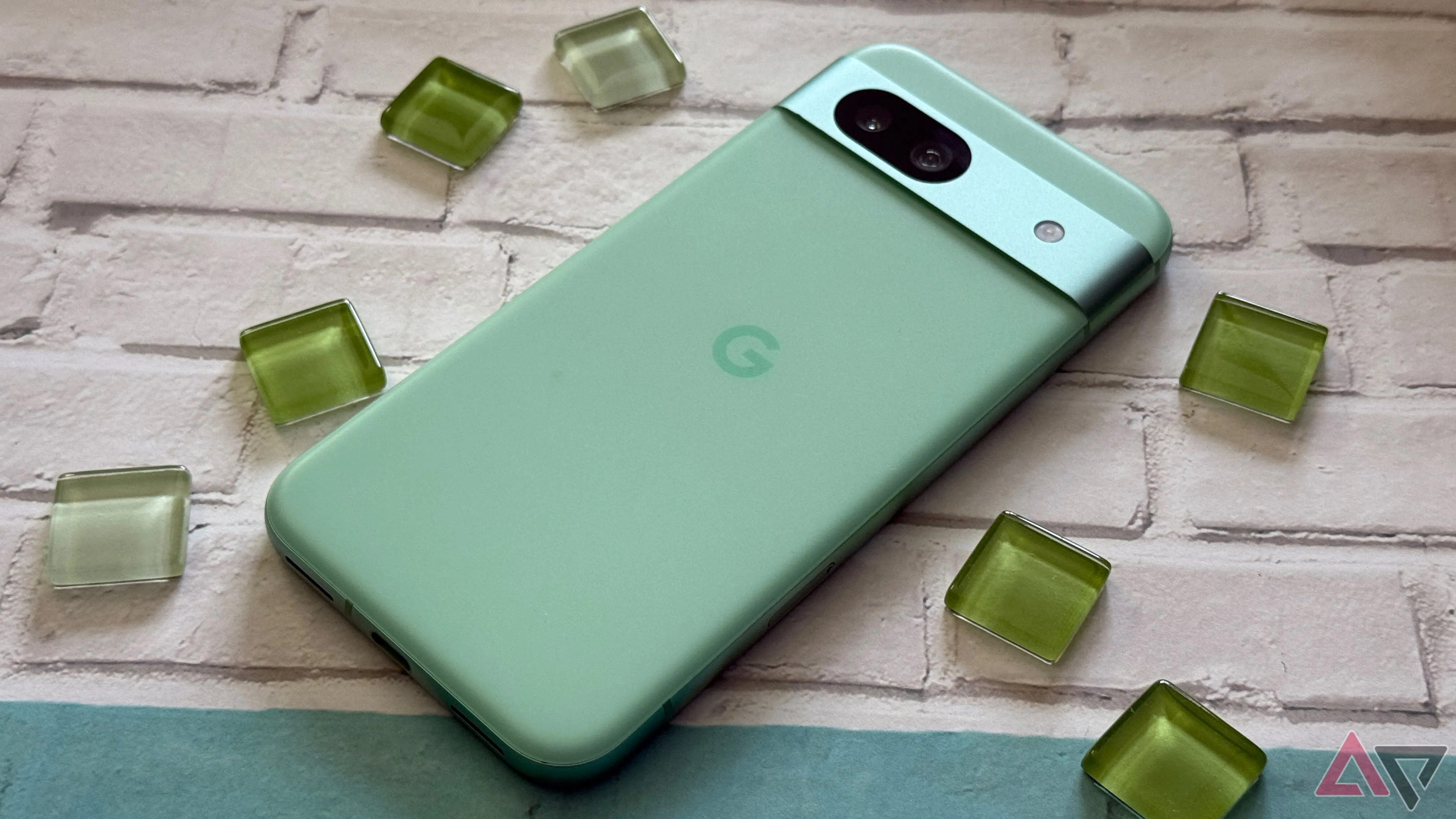 Google Pixel 8a phiên bản màu xanh lá, đặt trong không gian nghệ thuật với các hạt thủy tinh