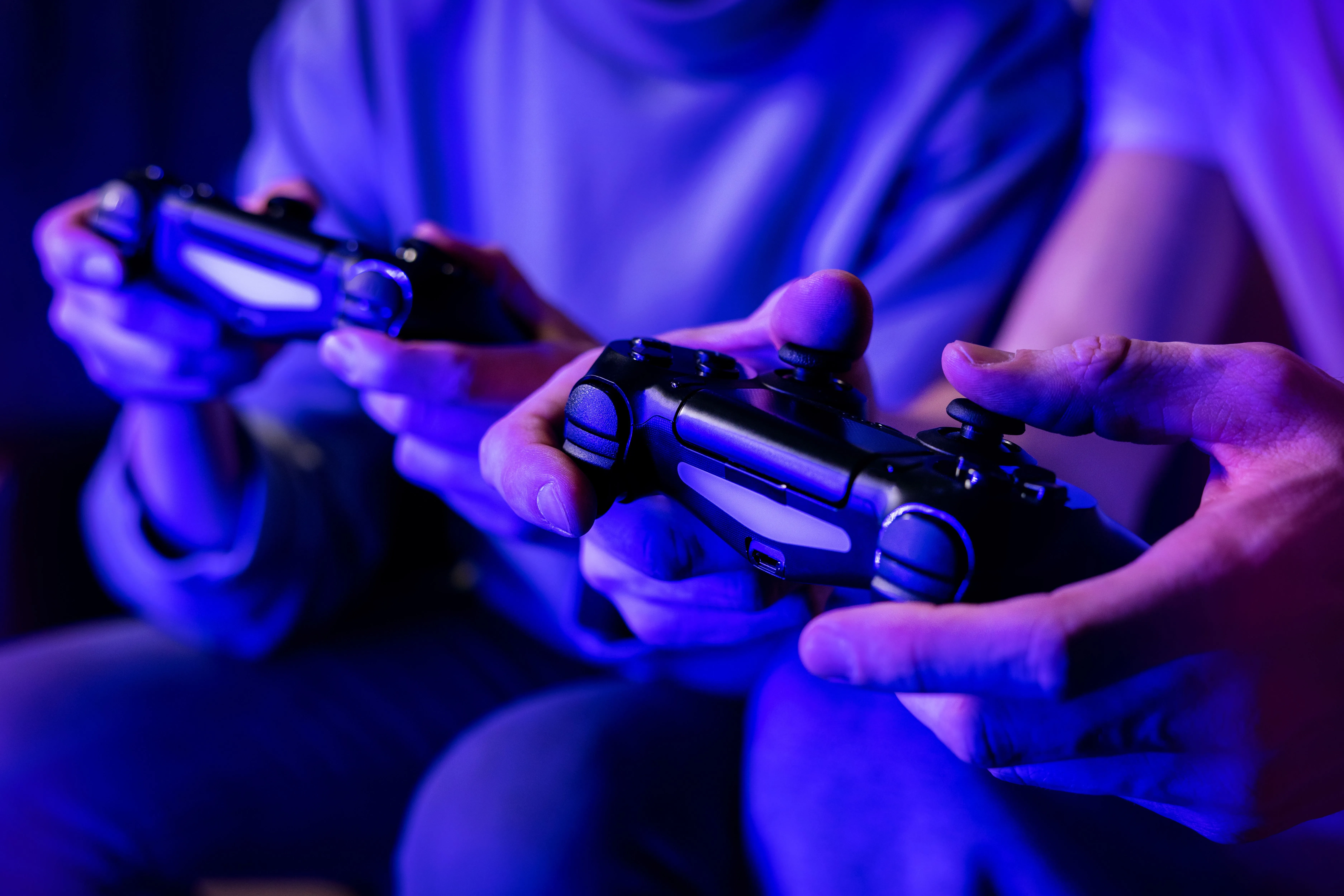 Hai người bạn đang vui vẻ chơi game nhiều người chơi trên ghế sofa, mỗi người cầm một tay cầm điều khiển, thể hiện sự thoải mái và nhạy bén của hệ thống điều khiển game.