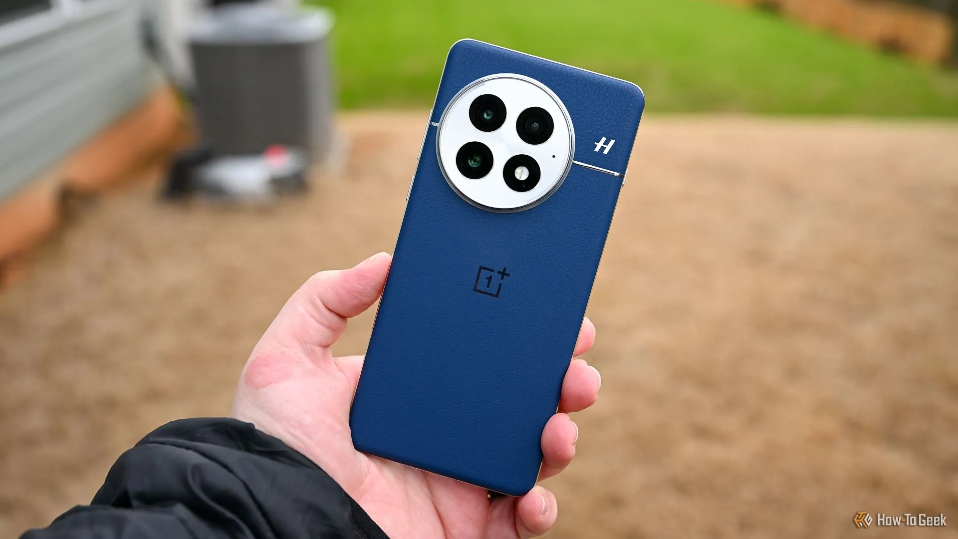 Hình ảnh người đang cầm điện thoại OnePlus 13 màu xanh, thể hiện mặt lưng và cụm camera