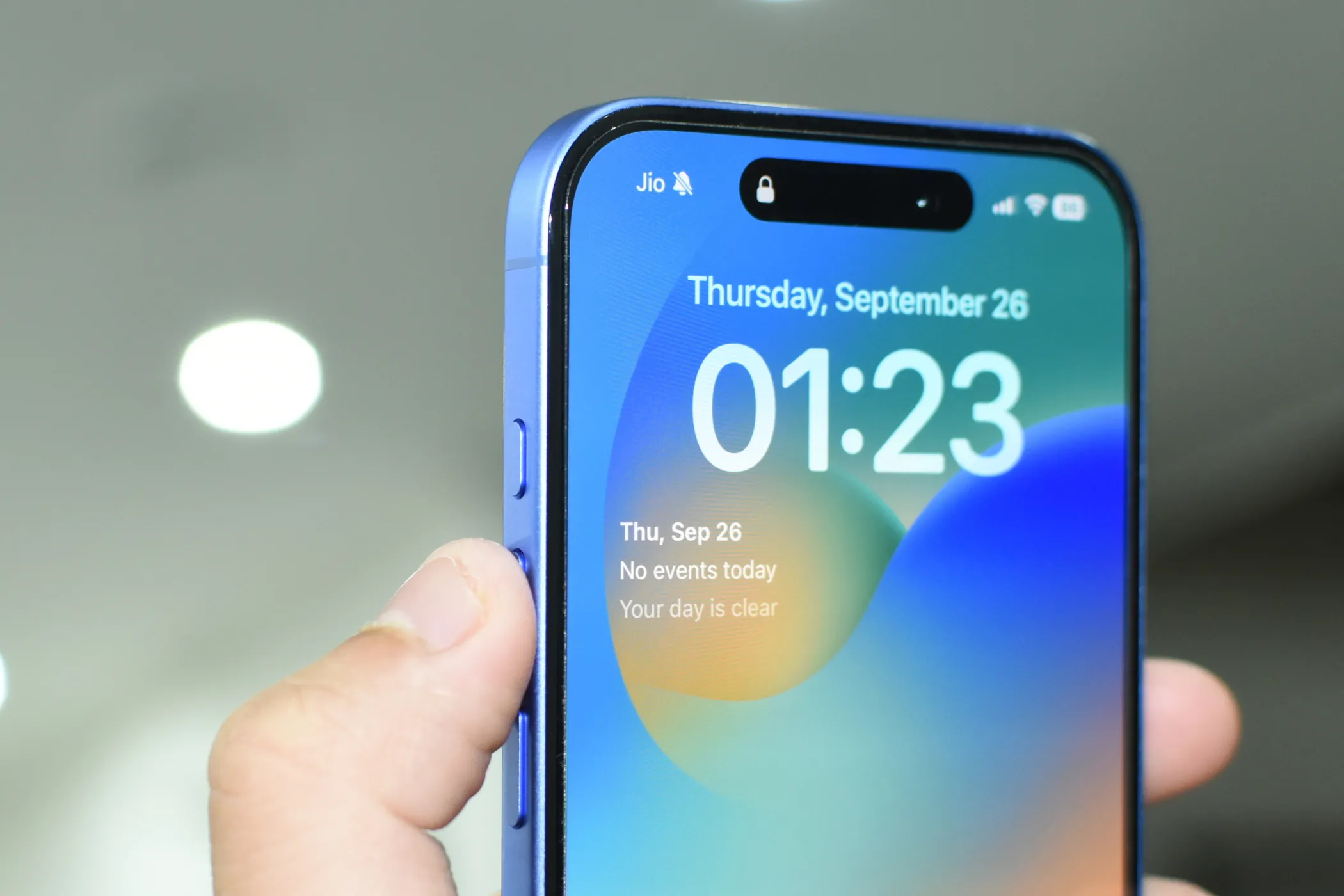 iPhone 16 màu xanh nước biển đậm với ngón cái chỉ vào Nút Tác vụ (Action Button) ở cạnh trái.