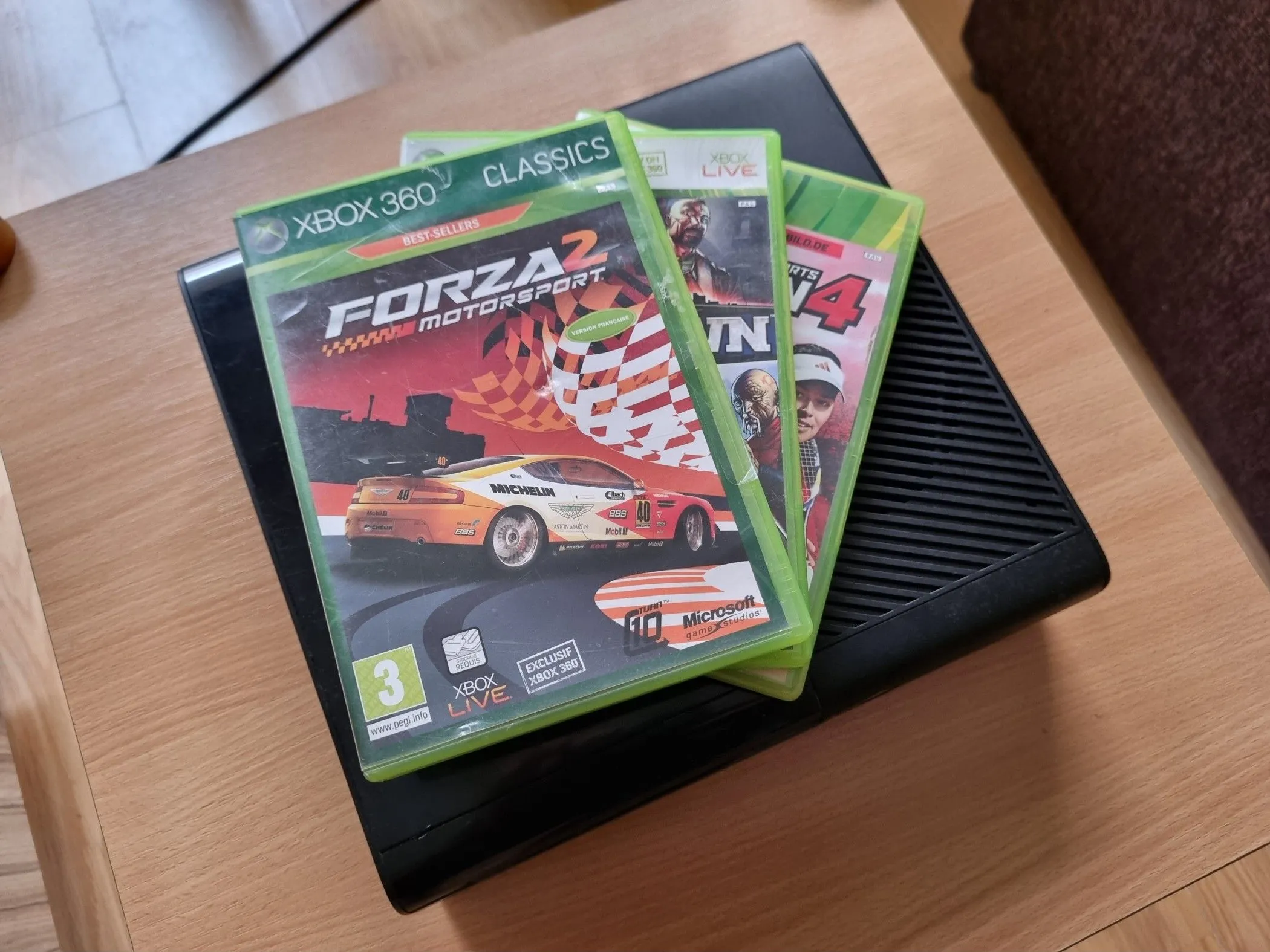 Máy chơi game Xbox 360 với những hộp game vật lý xếp chồng lên nhau, thể hiện sự đa dạng của thư viện game giá rẻ.