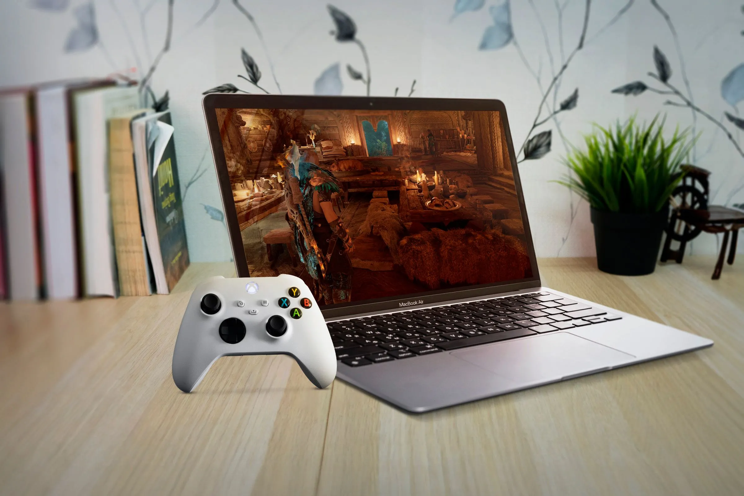 Một chiếc MacBook Air được đặt dưới bàn gỗ, màn hình hiển thị trò chơi và tay cầm Xbox, gợi ý về tiềm năng của một Mac chuyên biệt cho gaming