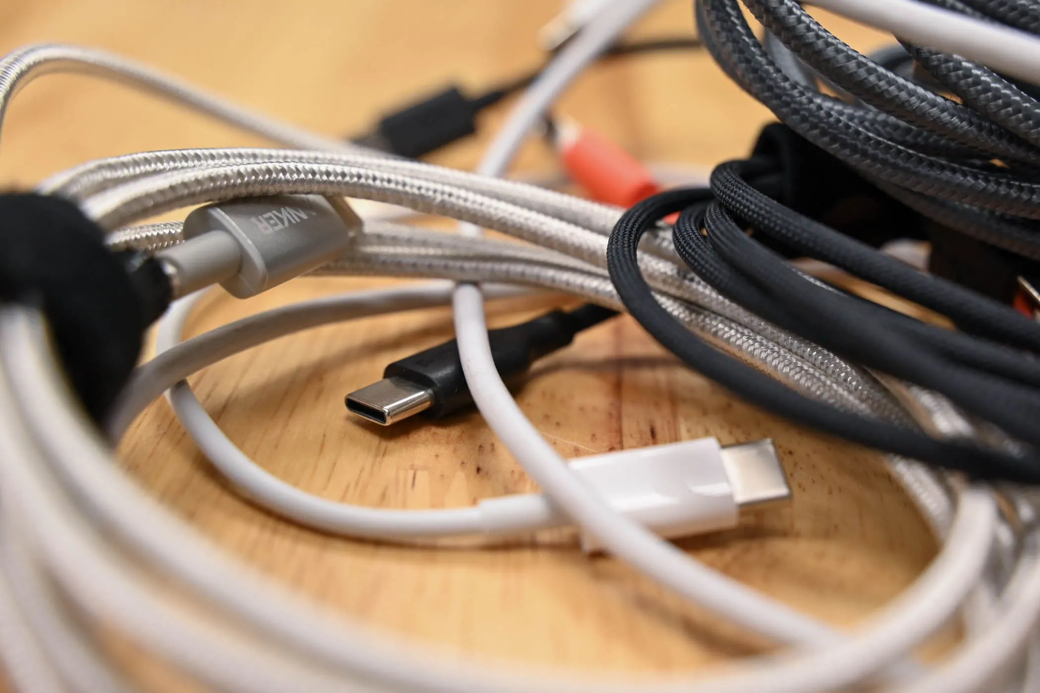 Một chồng cáp USB-C, Lightning và Micro-USB lộn xộn trên mặt bàn gỗ, thể hiện thách thức trong việc quản lý dây sạc hàng ngày