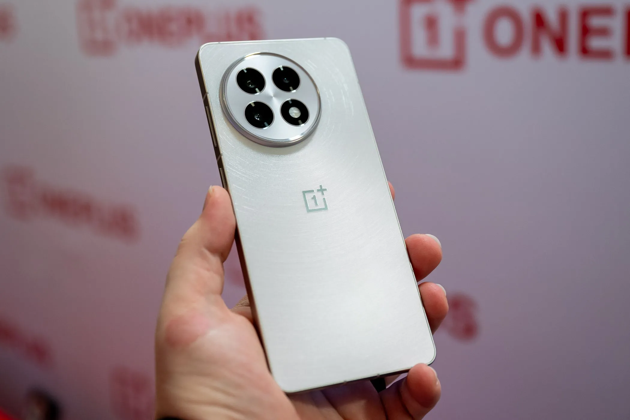 Người dùng đang cầm chiếc điện thoại OnePlus 13R màu trắng, làm nổi bật thiết kế tổng thể và dung lượng pin lớn.