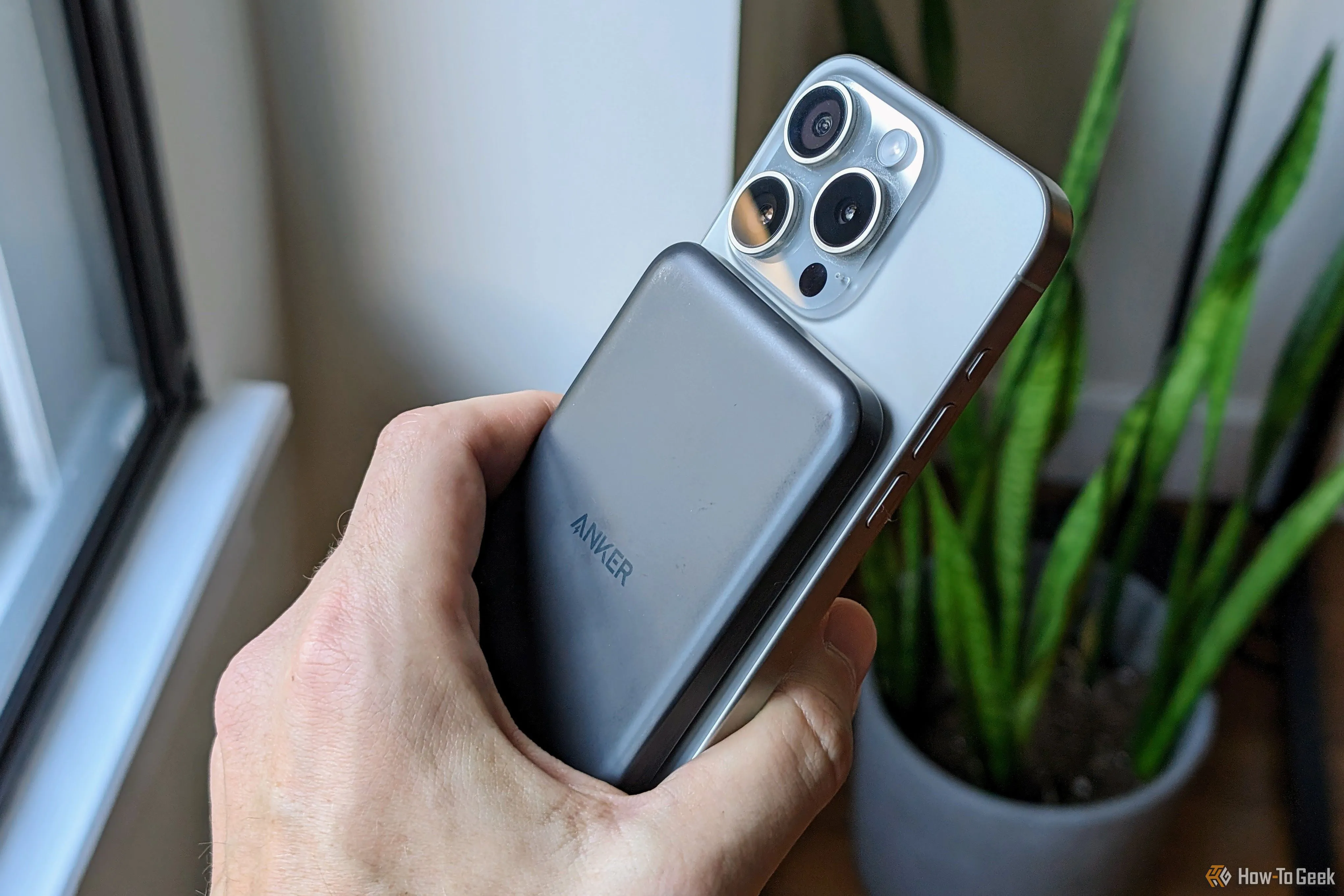 Pin dự phòng Anker MagGo gắn từ tính vào mặt lưng iPhone 15 Pro, thể hiện khả năng sạc và sử dụng điện thoại cùng lúc.