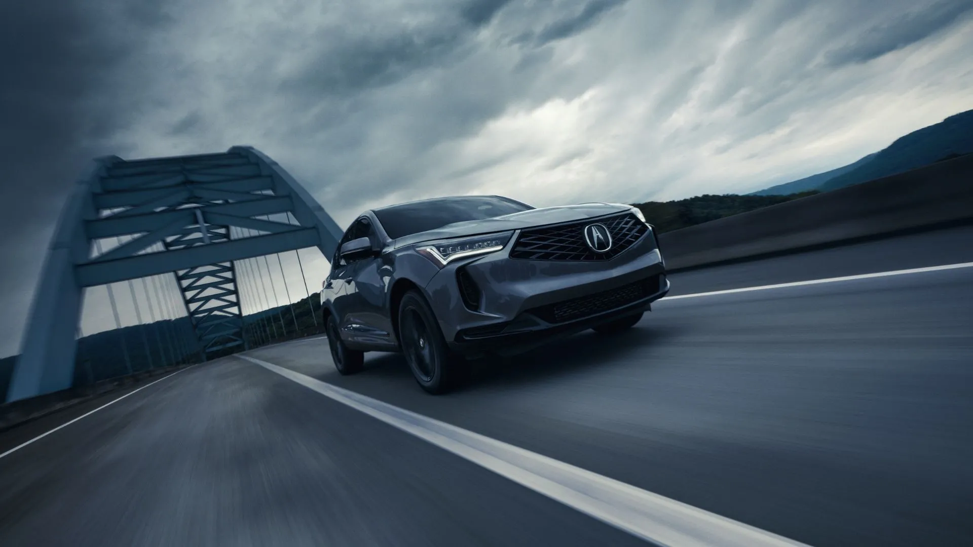 Acura RDX Technology Package 2025 màu xám bạc mạnh mẽ di chuyển trên cầu dưới bầu trời u ám, mang lại hiệu suất vượt trội