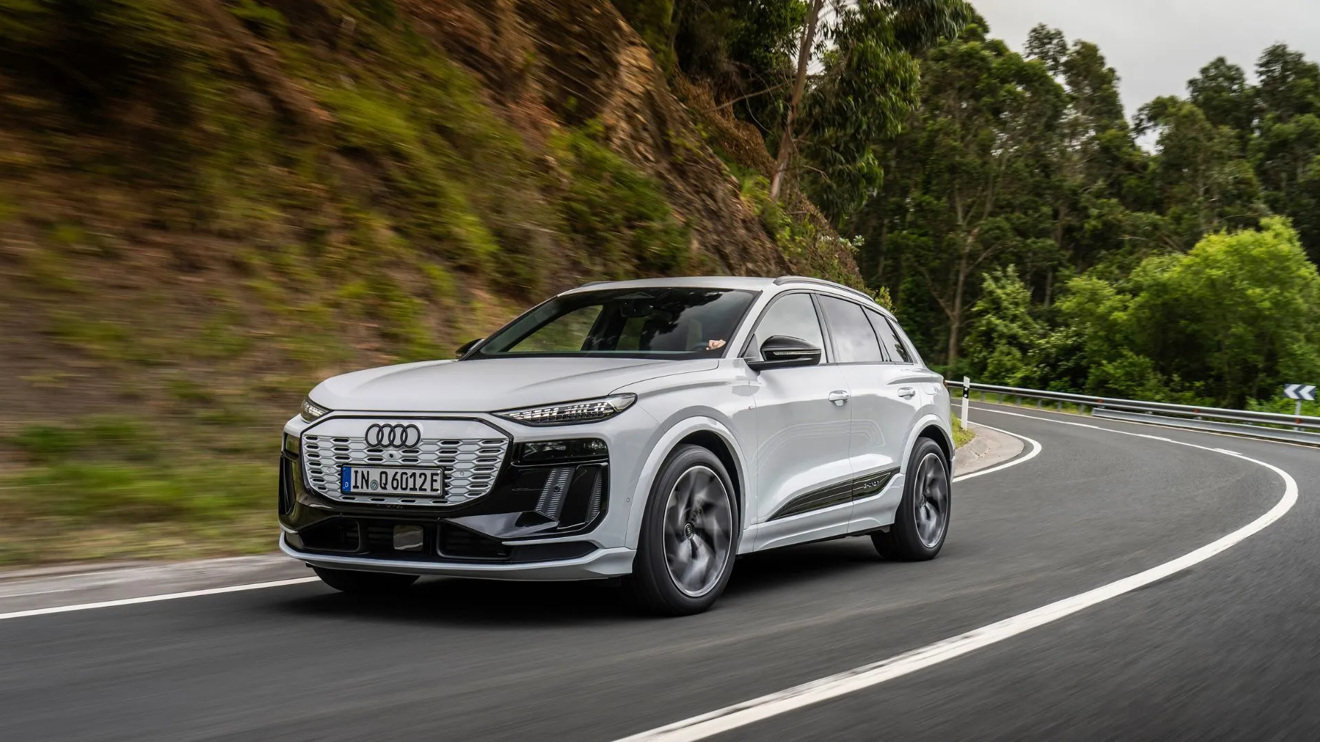Audi Q6 e-tron màu trắng di chuyển trên đường đồi núi uốn lượn, nhấn mạnh khả năng vận hành của SUV điện