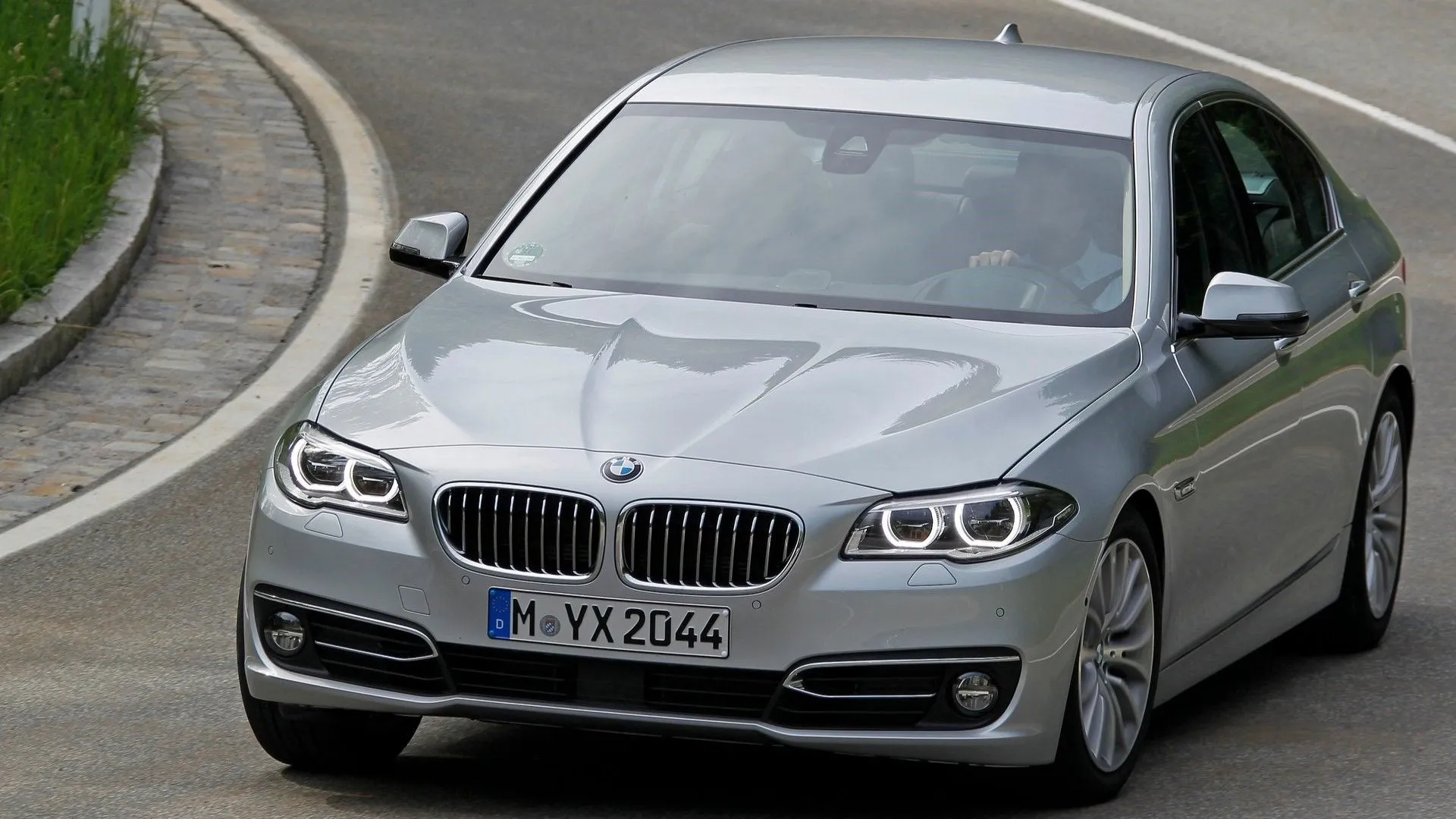 BMW 5-Series đời 2014 màu xám đang di chuyển trên đường, góc chụp 3/4 phía trước
