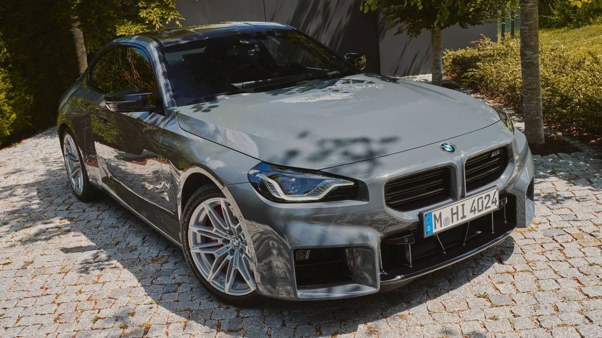 BMW M2 2025 màu xám đỗ trên con đường lát đá, thể hiện phong cách thể thao mạnh mẽ