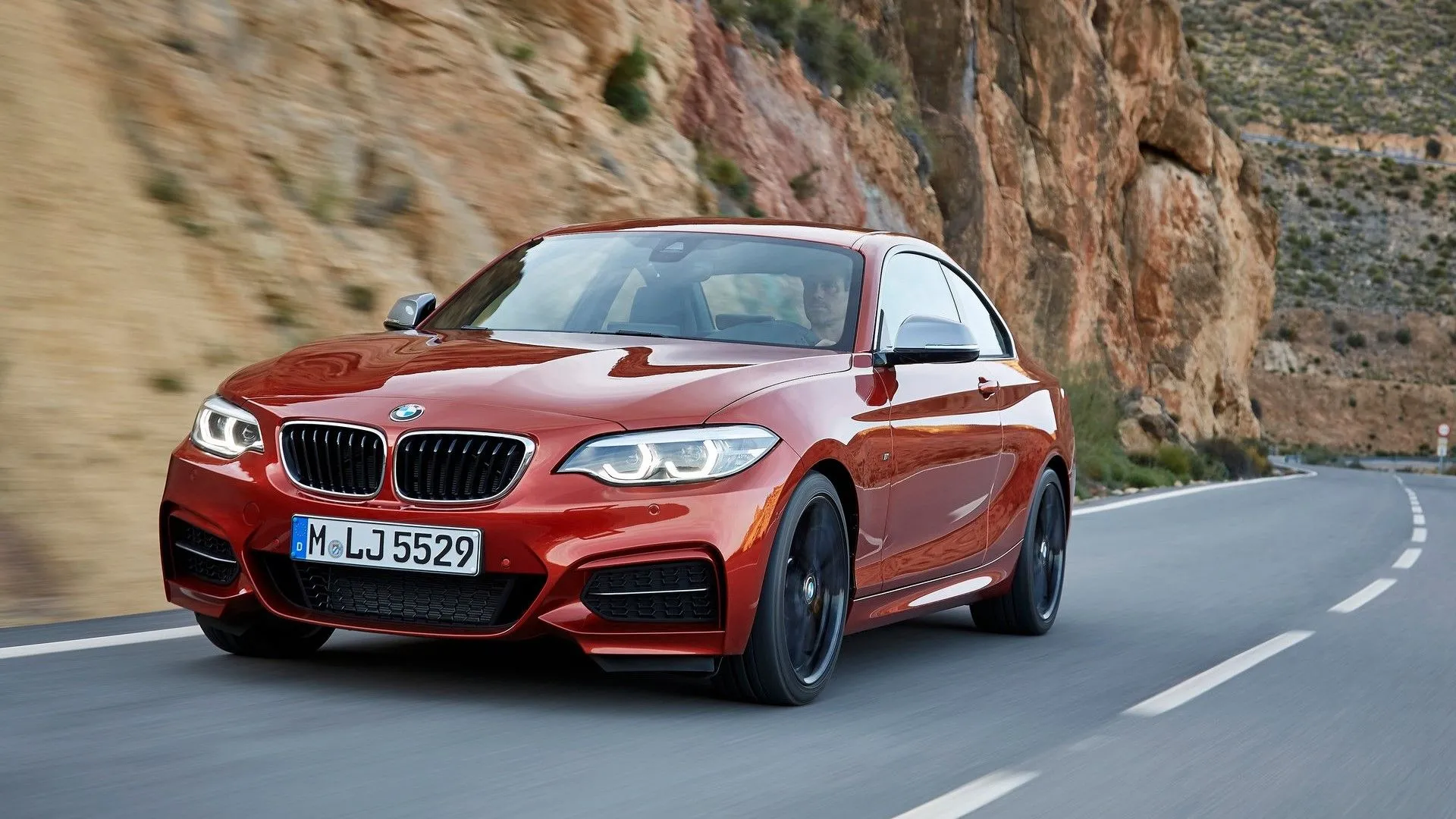 BMW M240i Coupe 2018 màu xanh dương đang vào cua, nổi bật với khung gầm thể thao và động cơ mạnh mẽ