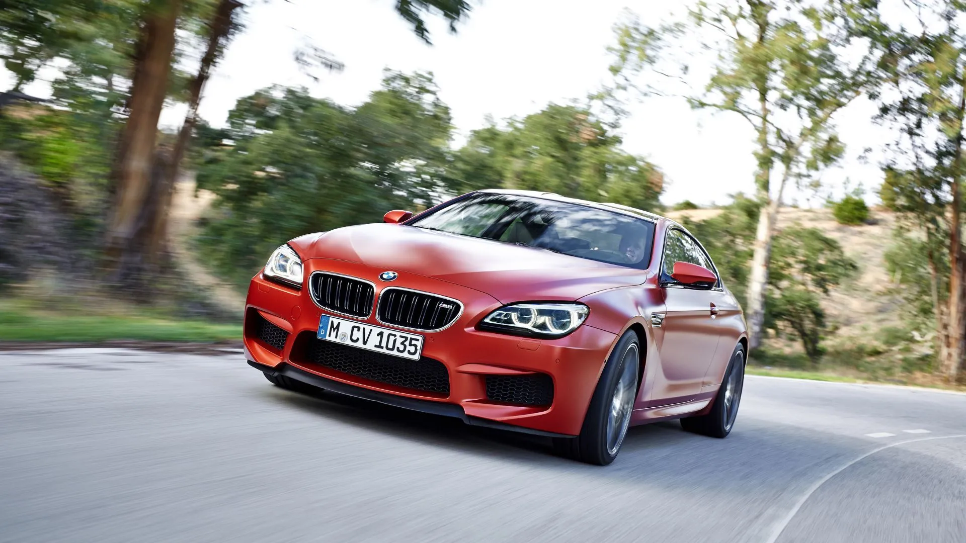 BMW M6 Coupe (F13) màu cam đang di chuyển trên con đường nông thôn quanh co, sự kết hợp hoàn hảo giữa hiệu suất và sang trọng