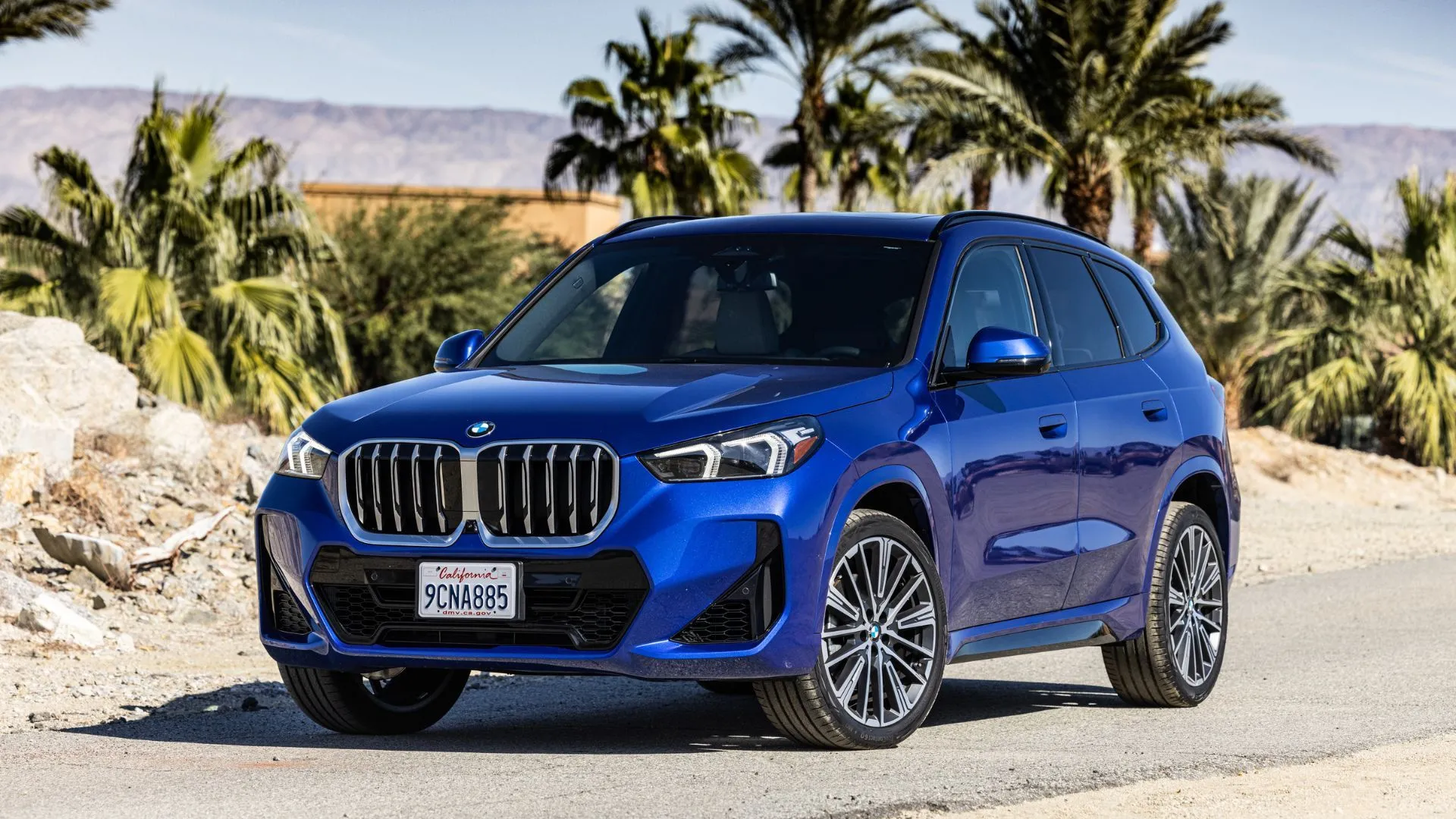 BMW X1 xDrive28i 2025 màu xanh dương năng động với hàng cọ phía sau, mang lại trải nghiệm lái thể thao cho gia đình