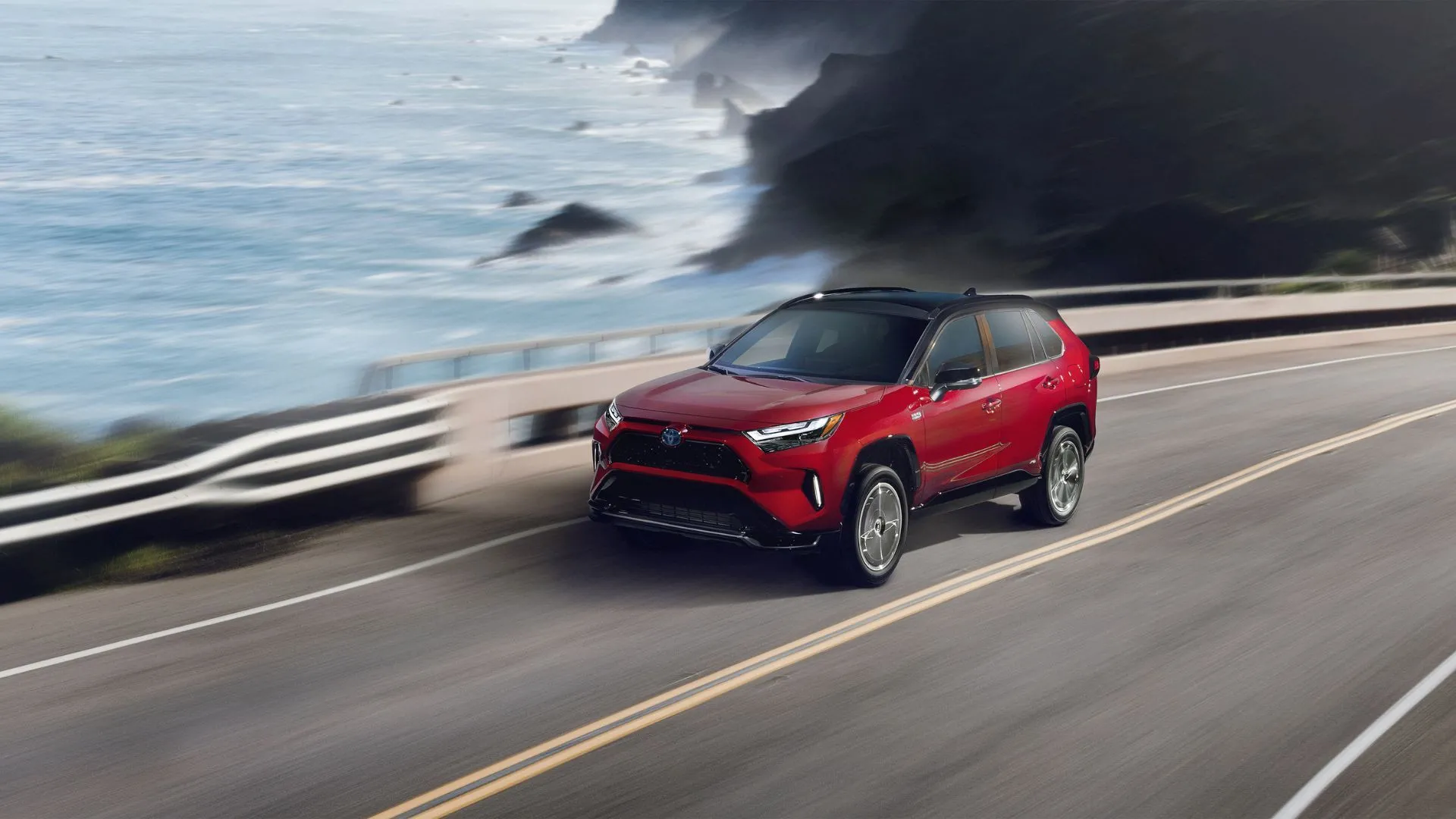Chiếc Toyota RAV4 Prime XSE 2024 màu đỏ đang chạy trên con đường ven biển, phía xa là đại dương bao la