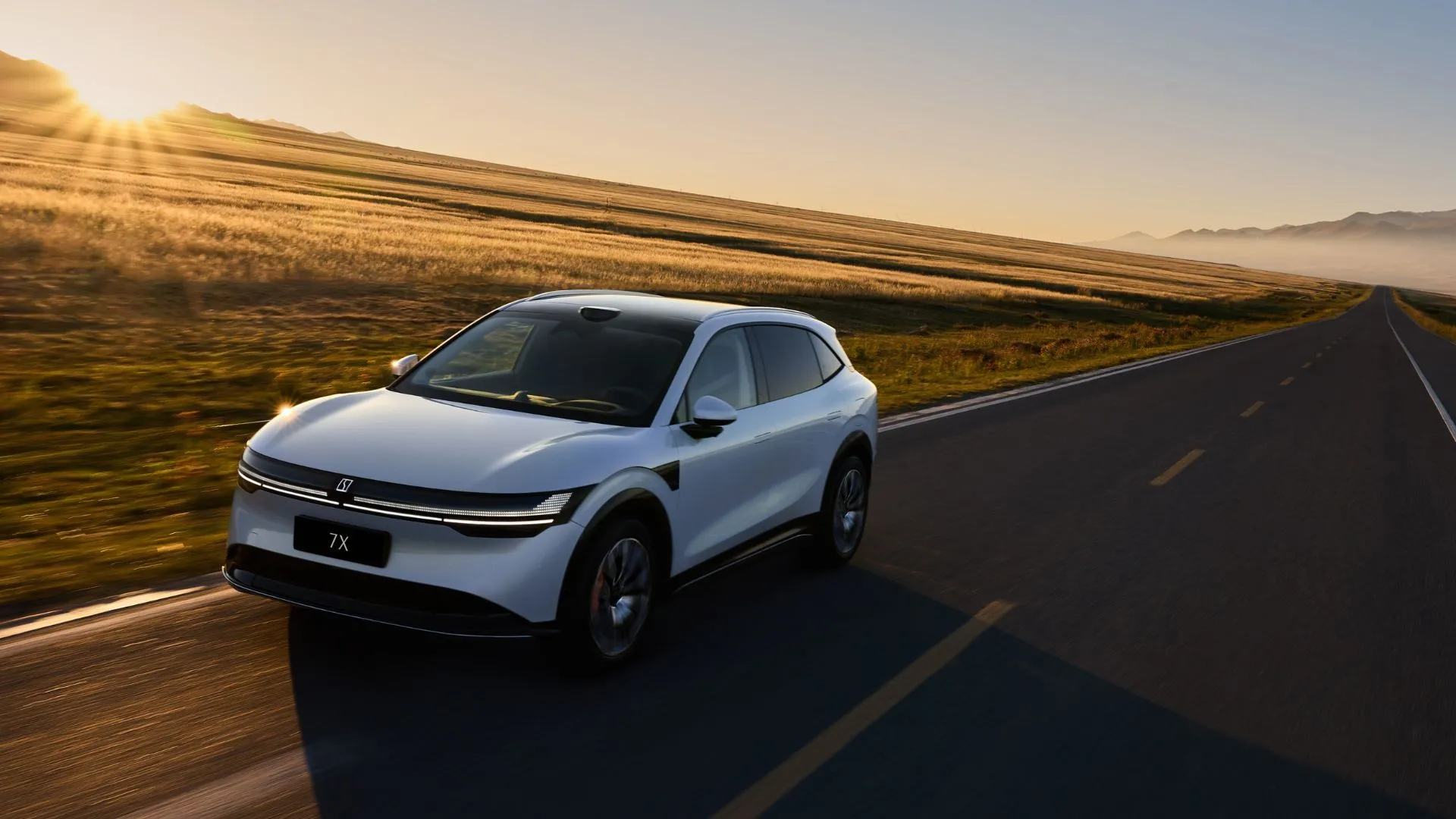Crossover điện Zeekr 7X màu bạc đang di chuyển trên con đường nông thôn lúc hoàng hôn, với thiết kế hiện đại và thanh lịch.