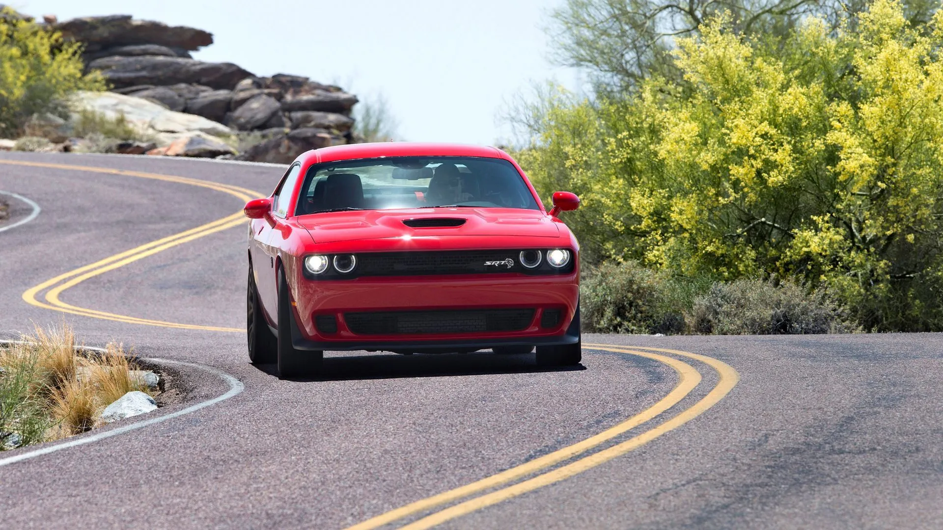 Dodge Challenger SRT Hellcat 2018 màu đỏ đang lái trên đường nông thôn quanh co, sức mạnh cơ bắp Mỹ không thể nhầm lẫn