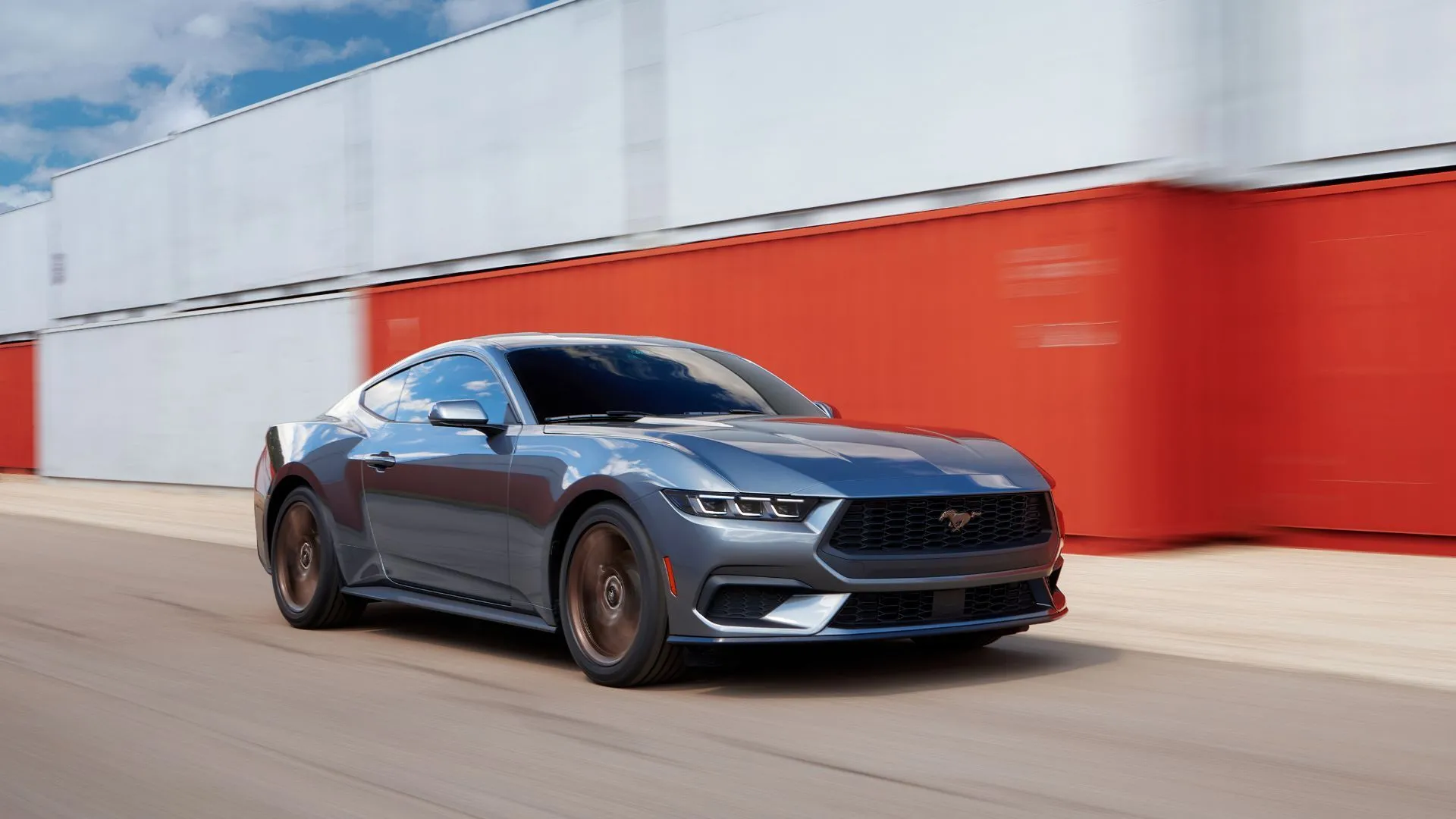 Ford Mustang 2025 màu xám bạc lướt qua các container vận chuyển, biểu tượng xe cơ bắp Mỹ vẫn giữ tùy chọn động cơ V8 và hộp số sàn.