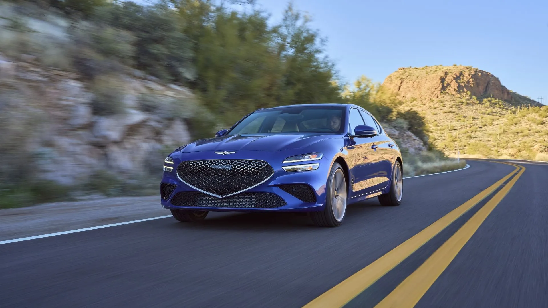 Genesis G70 2025 màu xám bạc đang chạy trên đường, thể hiện thiết kế thể thao và sang trọng