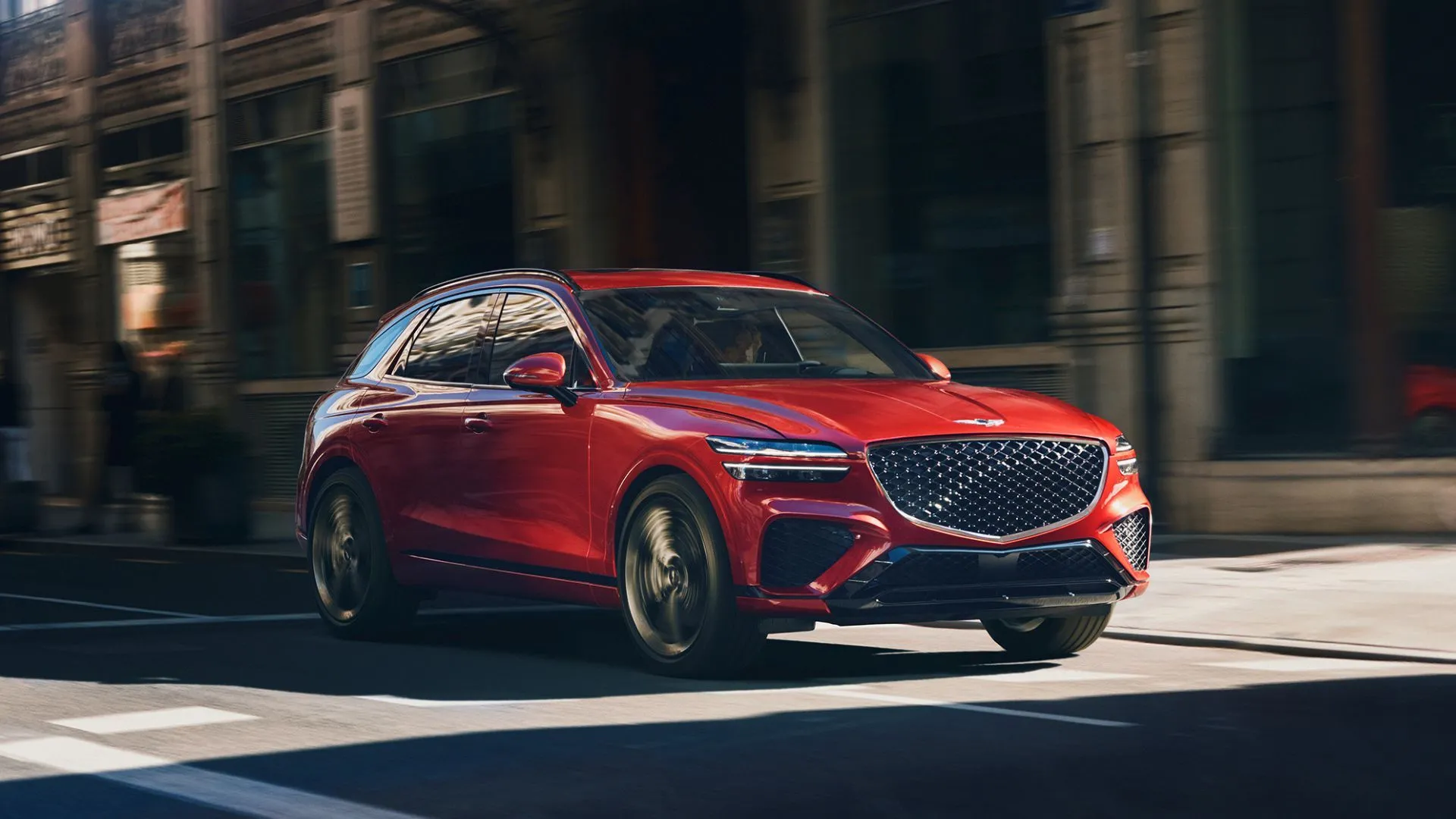Genesis GV70 2.5T Advanced AWD màu đỏ rực rỡ đang lướt qua thành phố, biểu tượng của sự sang trọng tinh tế