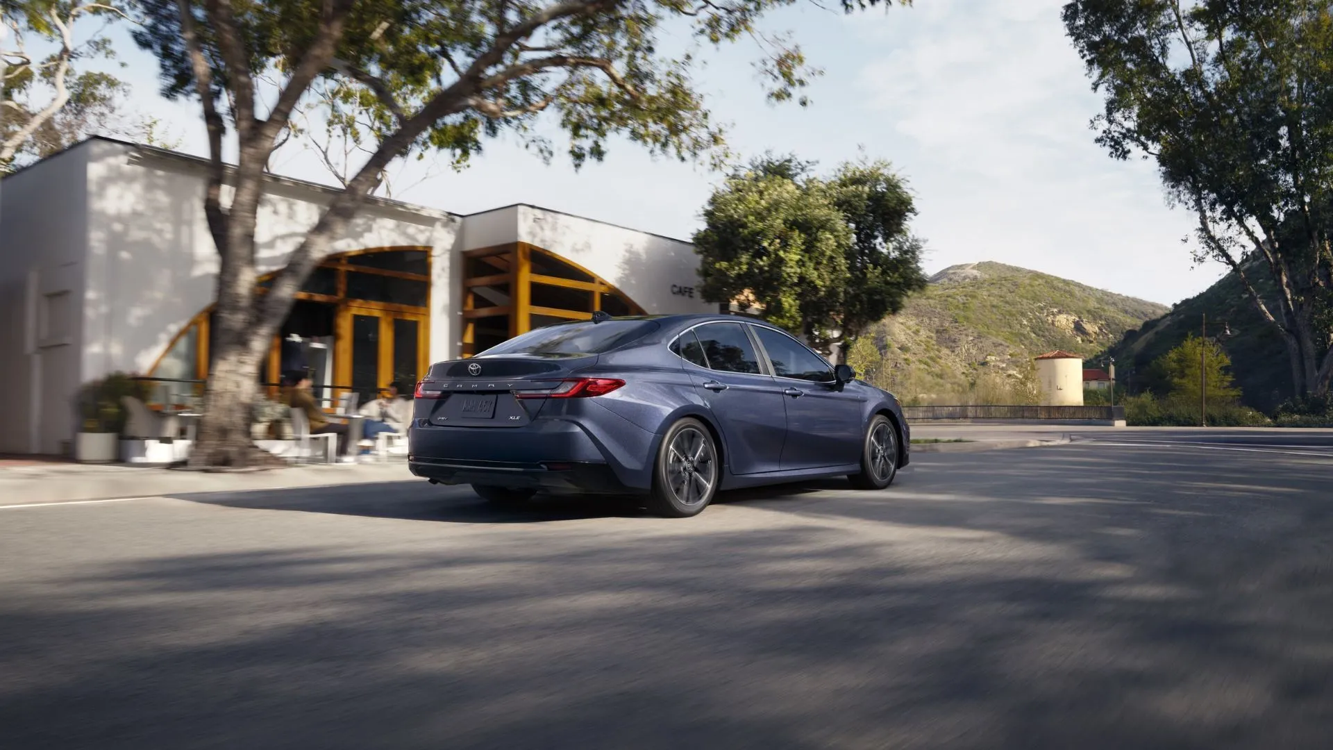 Góc nhìn 3/4 phía sau động của một chiếc Toyota Camry 2026 màu xám đang di chuyển qua thành phố