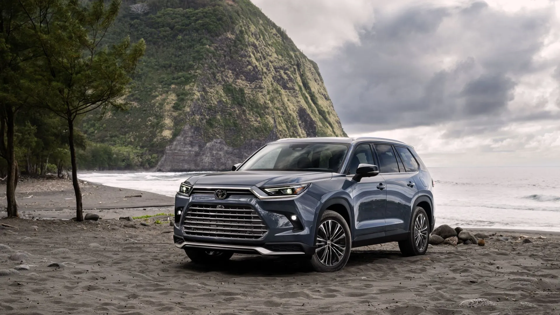 Hình ảnh chiếc SUV Toyota Grand Highlander 2025 màu xám bạc nhìn từ góc 3/4 phía trước, đậu trên đường nhựa