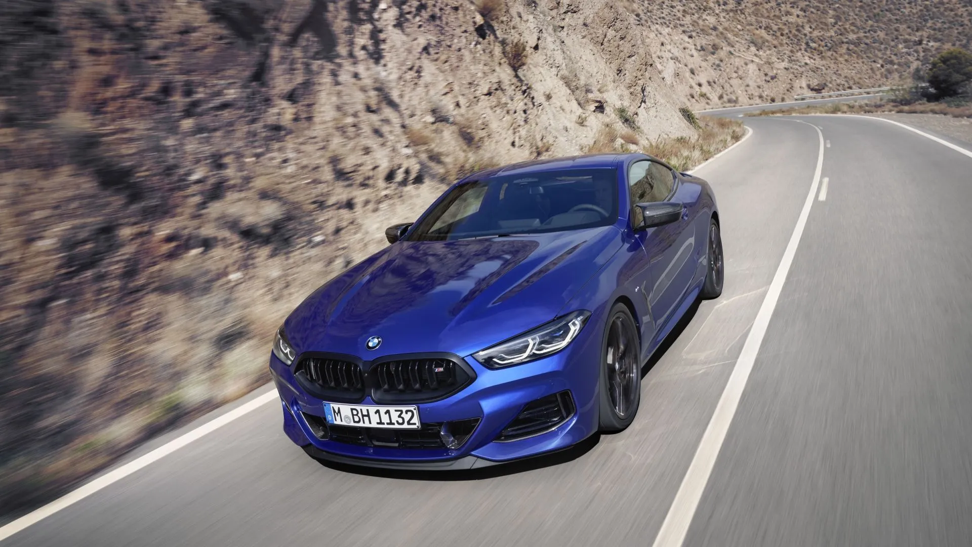 Hình ảnh góc 3/4 phía trước của BMW 8-Series 2025 màu xanh dương sẫm đang chạy trên đường