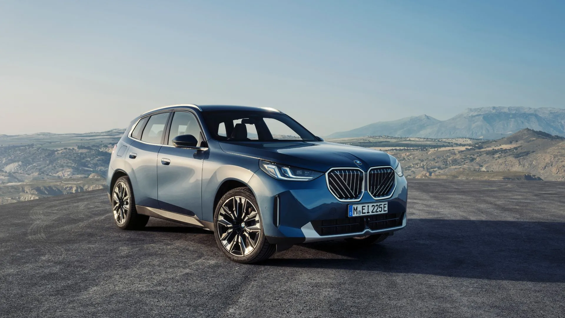 Hình ảnh góc 3/4 phía trước của BMW X3 30 xDrive 2025 màu xanh dương với núi non phía sau
