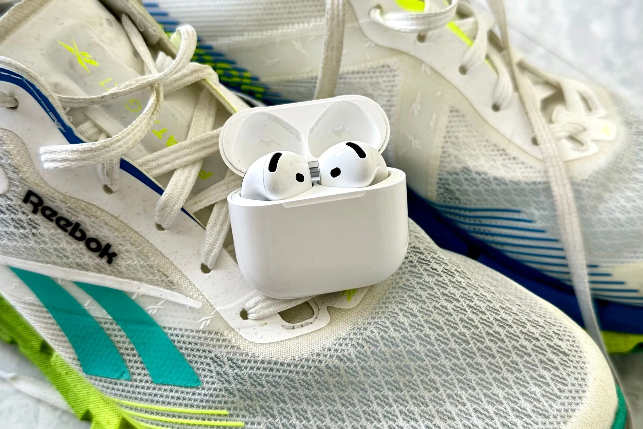 Hình ảnh tai nghe AirPods 4 đặt trên đôi giày thể thao, minh họa khả năng sử dụng thoải mái khi tập luyện hoặc chạy bộ