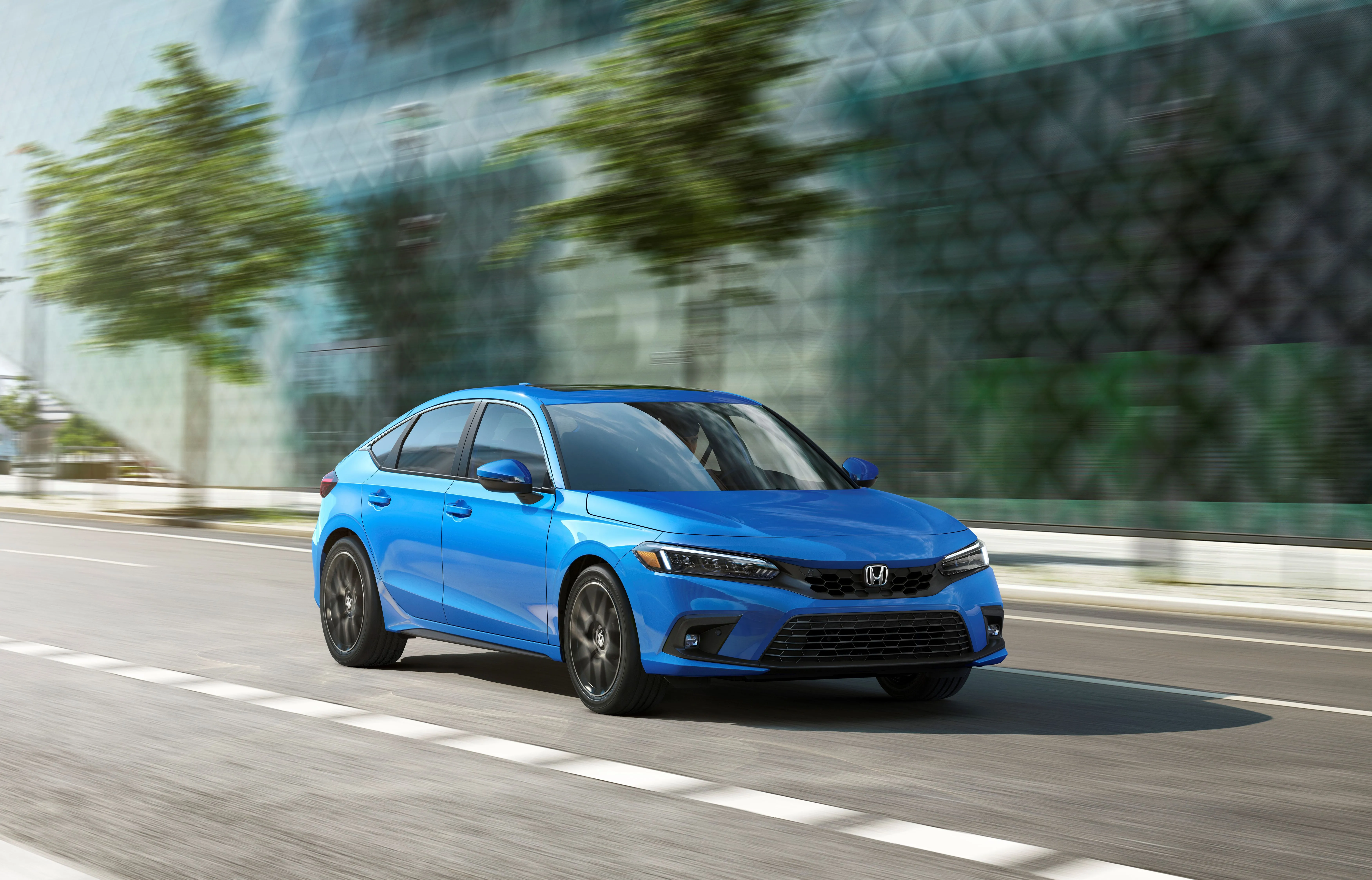 Honda Civic Hatchback màu xanh lam năng động đang lăn bánh trên đường phố, góc nhìn 3/4 từ phía trước.