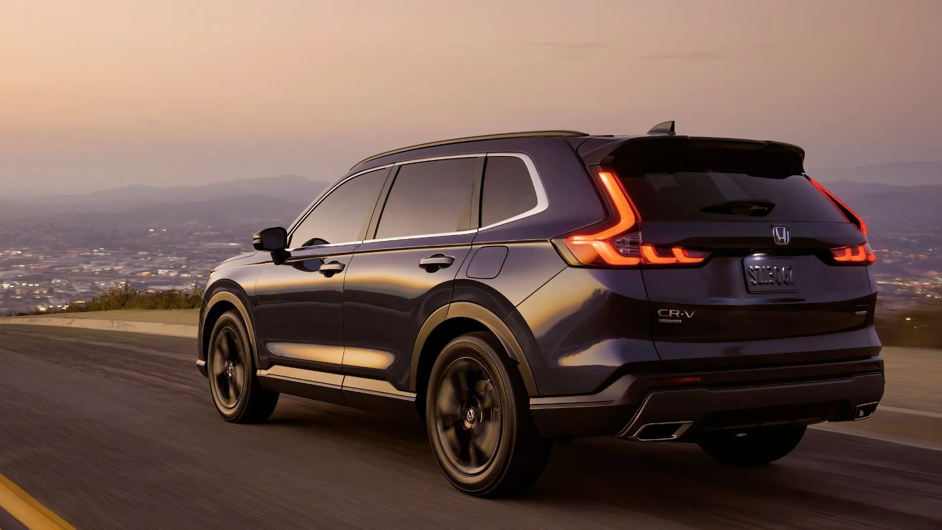 Honda CR-V Sport Touring màu xanh đậm 2023 đang di chuyển trên đường phố với ánh đèn đô thị lấp lánh phía sau, tôn lên vẻ sang trọng của phiên bản cao cấp