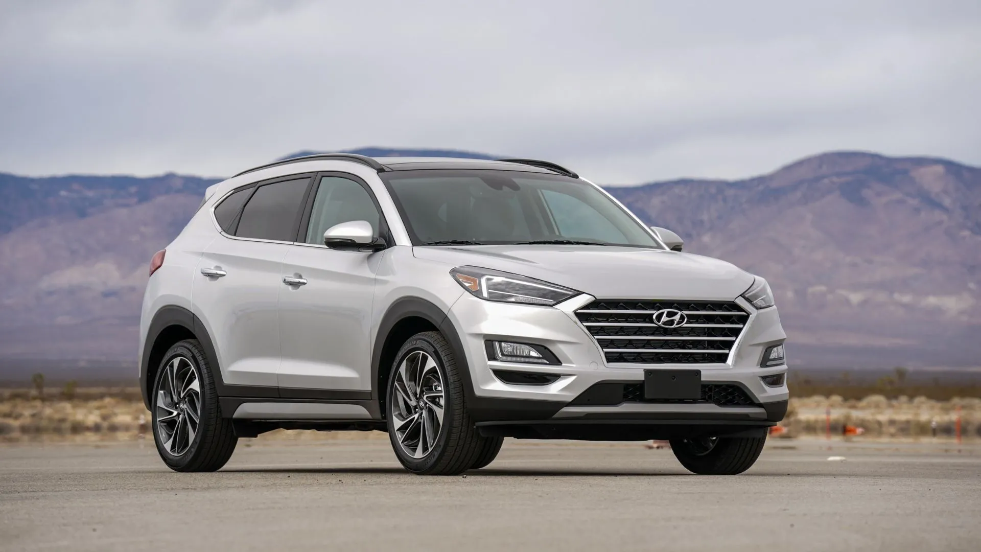 Hyundai Tucson Hybrid 2021 màu bạc đỗ trên nền nhựa đường với núi non hùng vĩ, thể hiện sự mạnh mẽ và linh hoạt của SUV Hybrid.