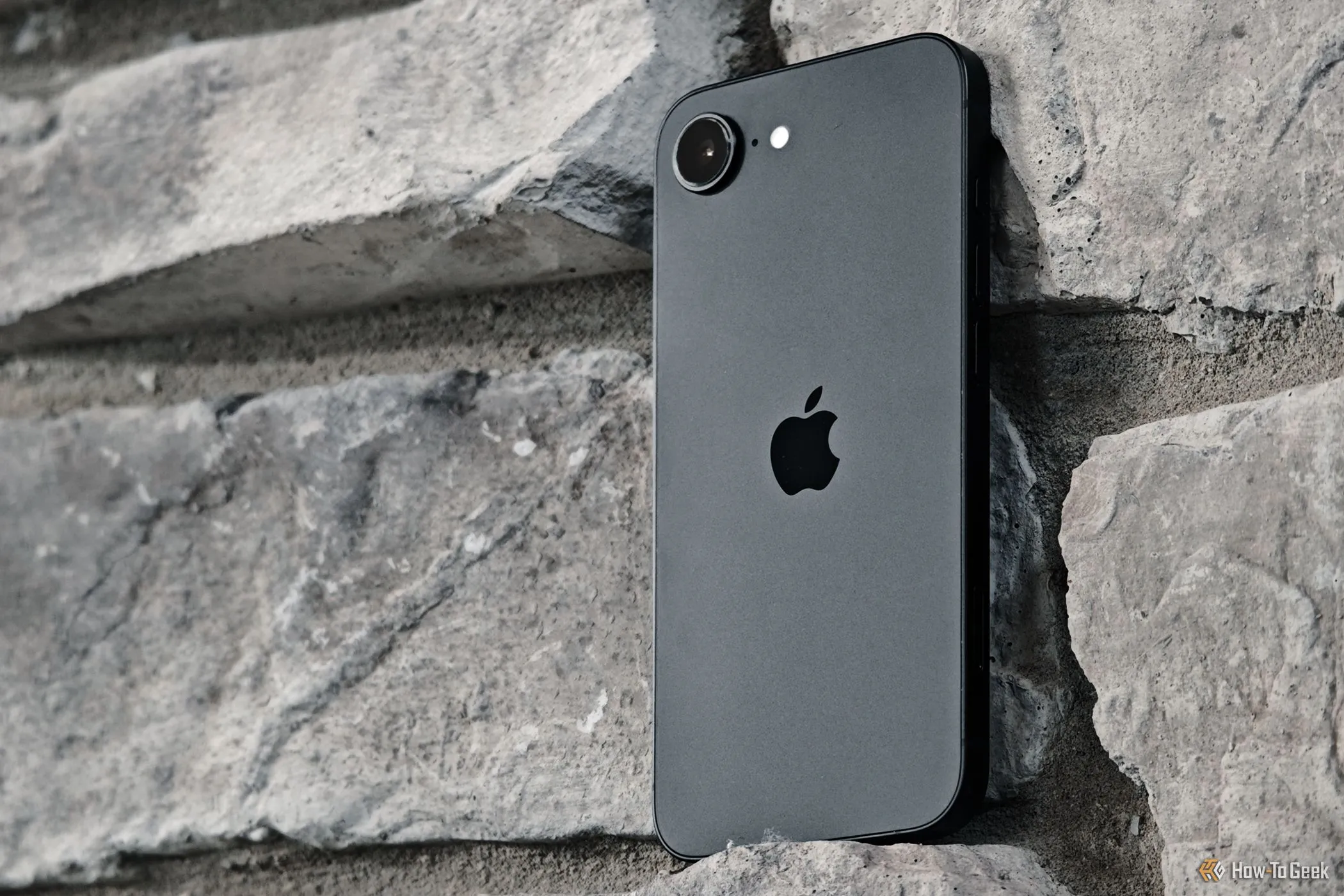 iPhone 16e màu trắng dựa vào tường gạch