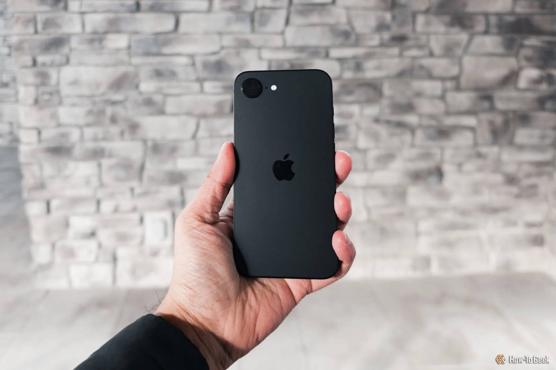 iPhone 16e màu trắng được cầm trên tay dựa vào tường xám