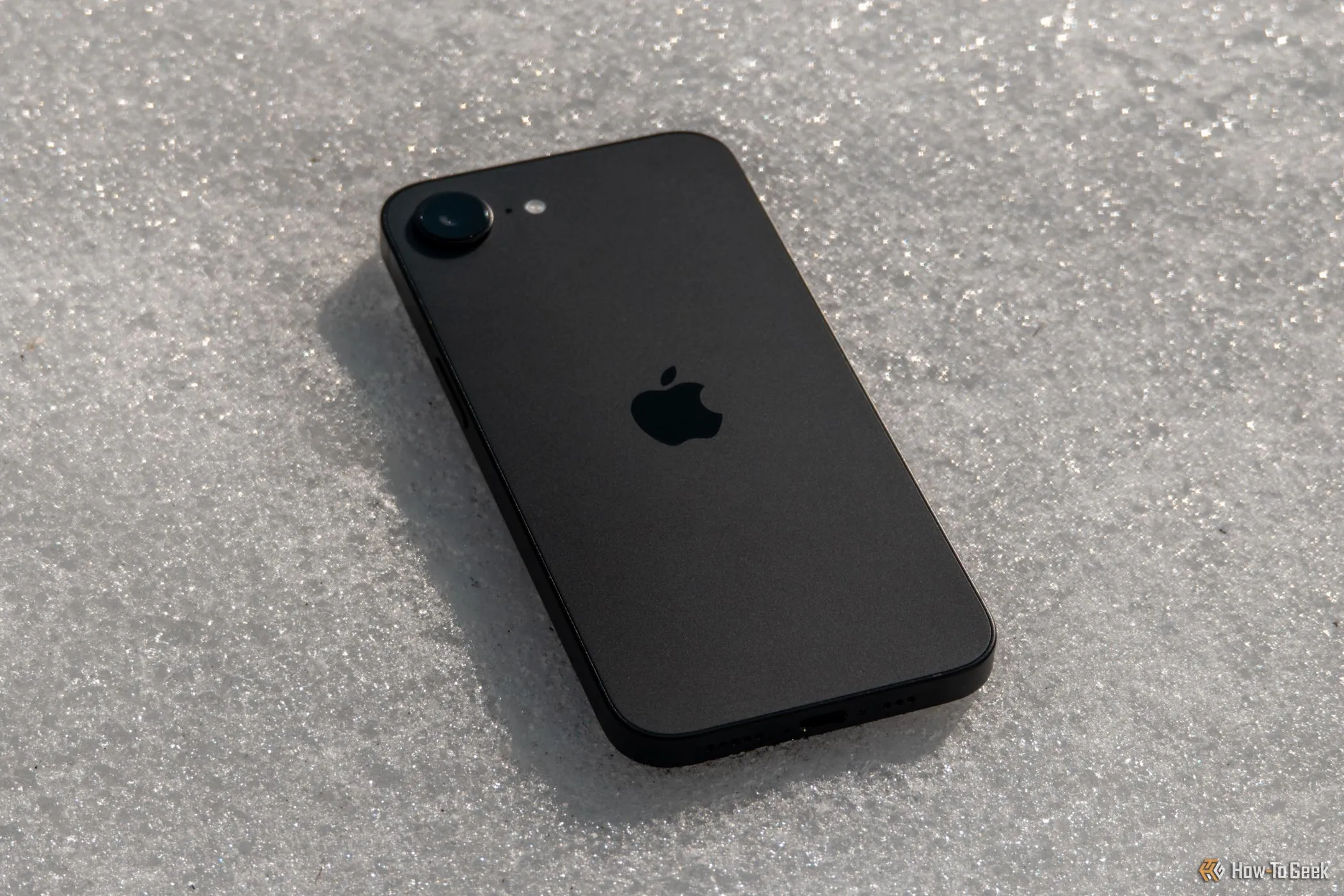 iPhone 16e màu trắng được đặt úp trên nền tuyết