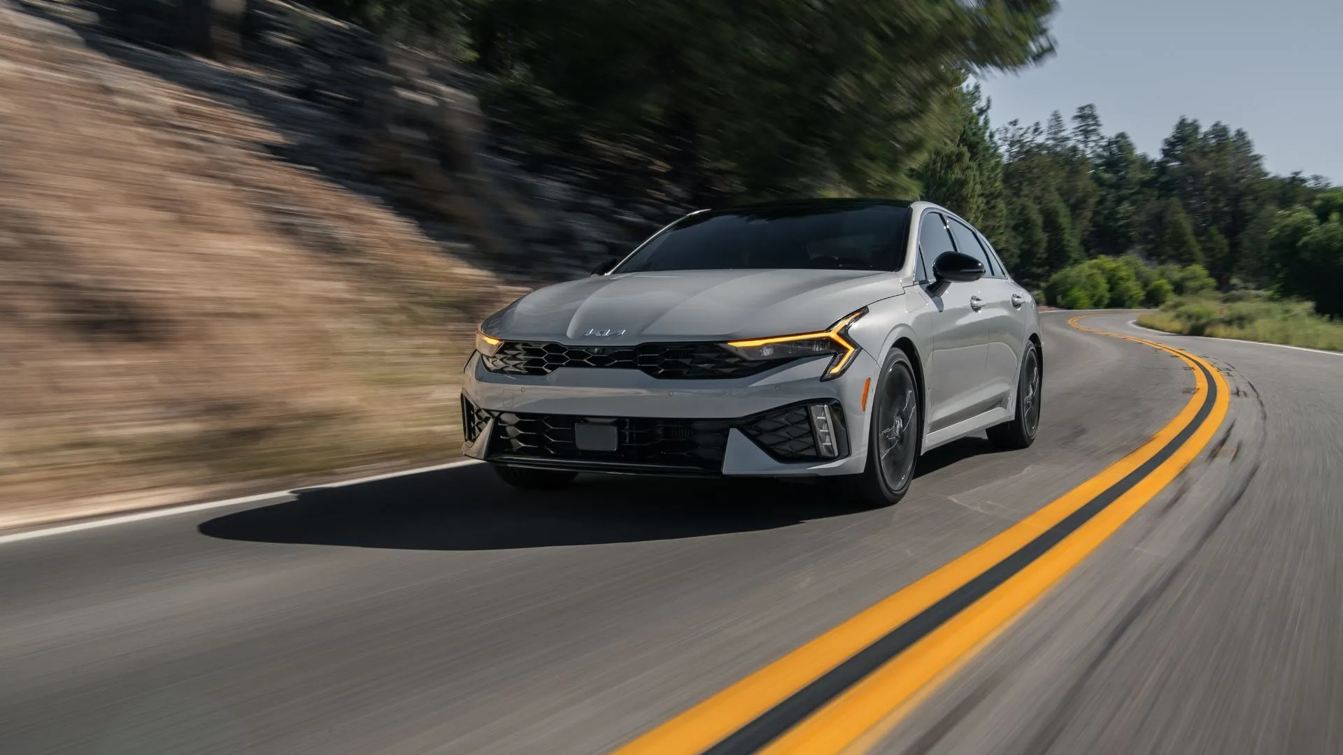 Kia K5 GT 2025 màu xám trên đường đèo, cho thấy thiết kế năng động và khả năng vận hành