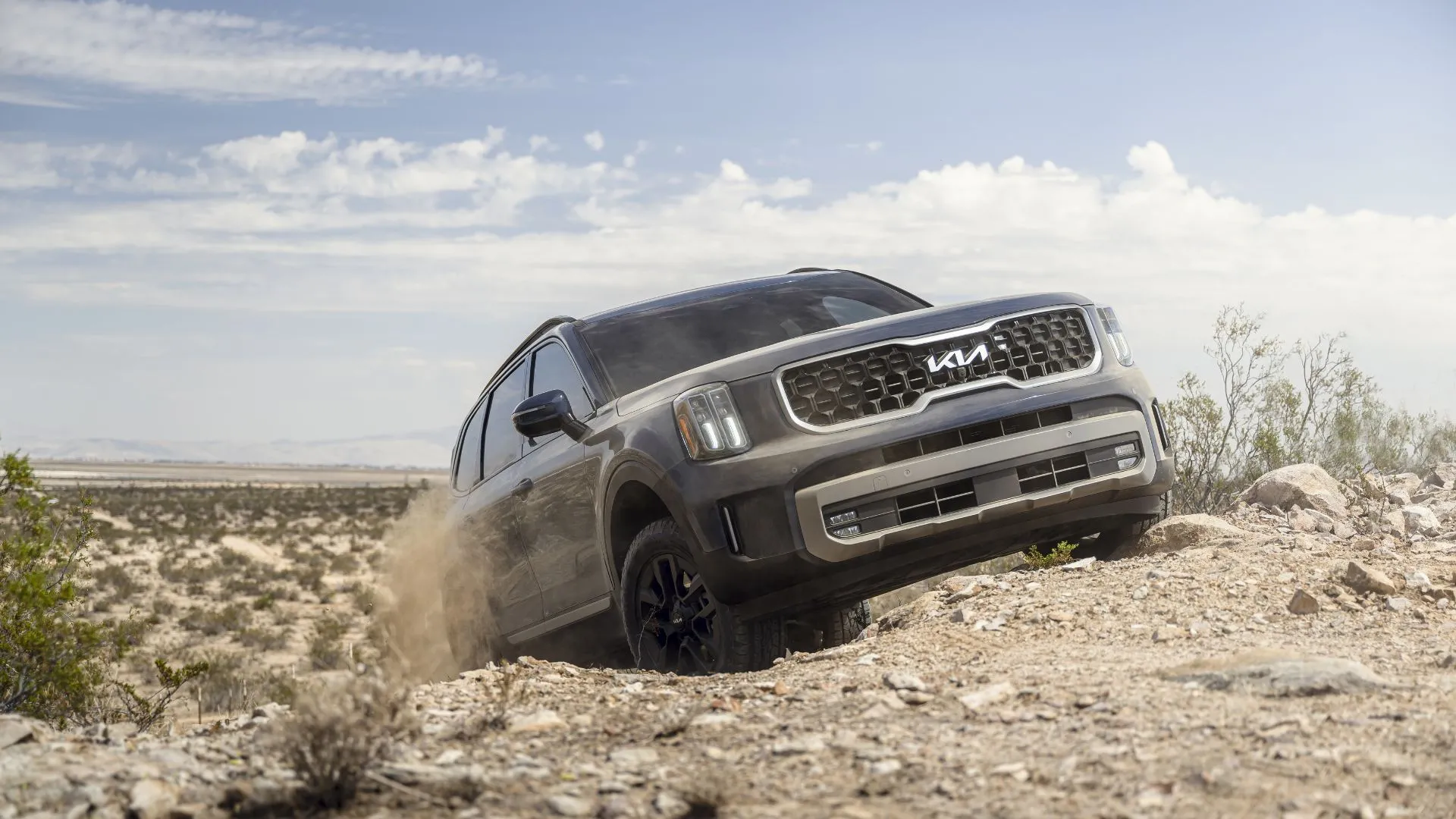 Kia Telluride 2023 màu xanh dương vận hành trên địa hình sa mạc đầy cát, minh họa khả năng vượt địa hình nhẹ của phiên bản X-Pro hoặc X-Line.