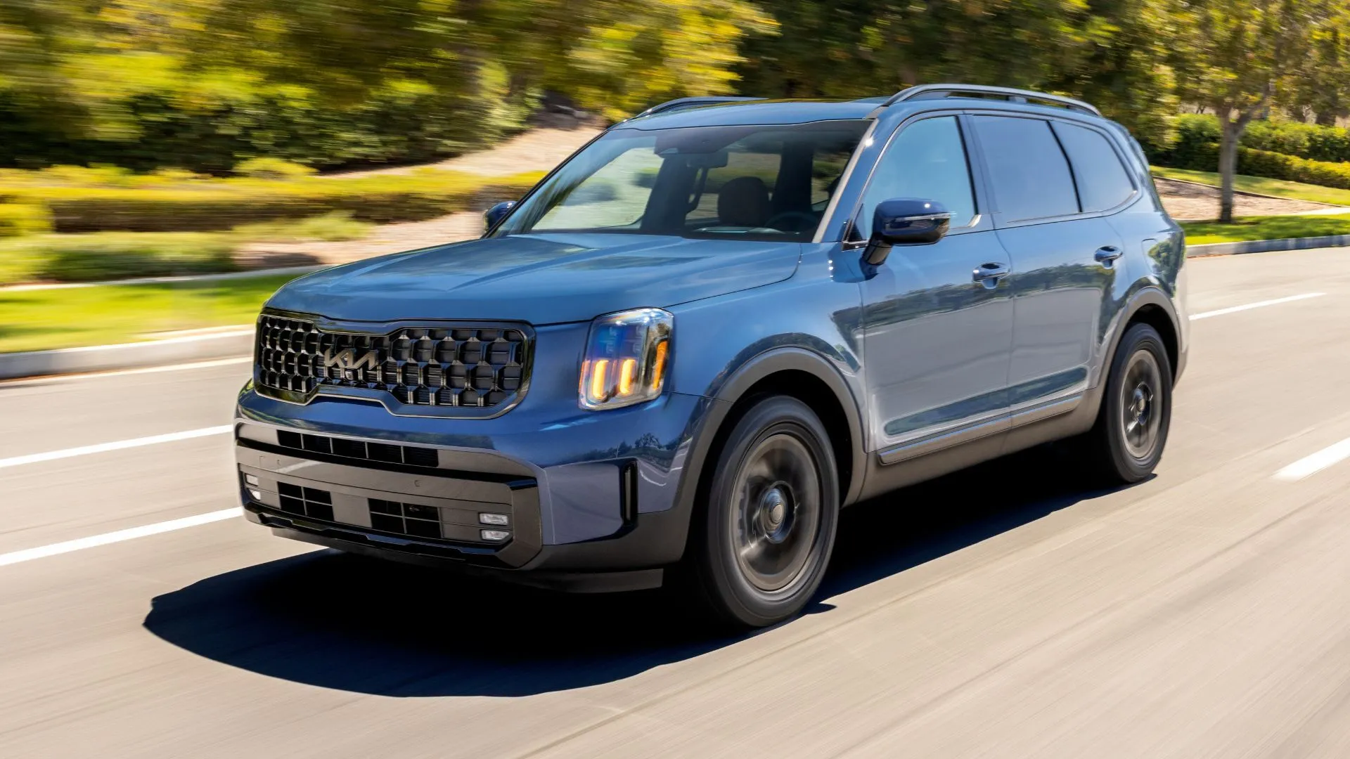 Kia Telluride 2025 màu xanh dương đang lướt đi trên con đường rợp bóng cây, nổi bật với thiết kế sang trọng và hiện đại.