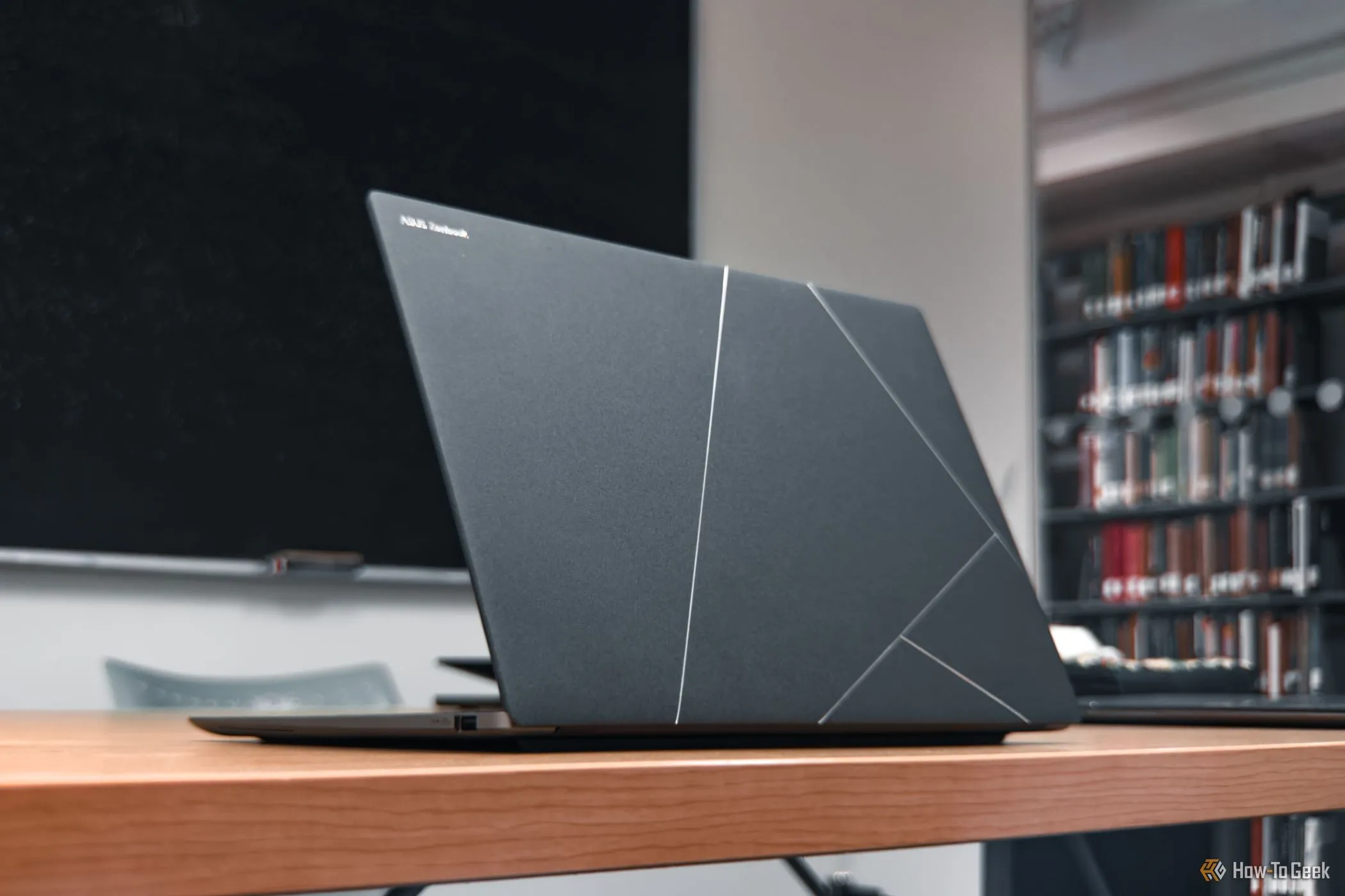 Laptop ASUS Zenbook S 14 màu xám Zumaia Gray mở nắp trên bàn gỗ, thể hiện thiết kế mỏng nhẹ