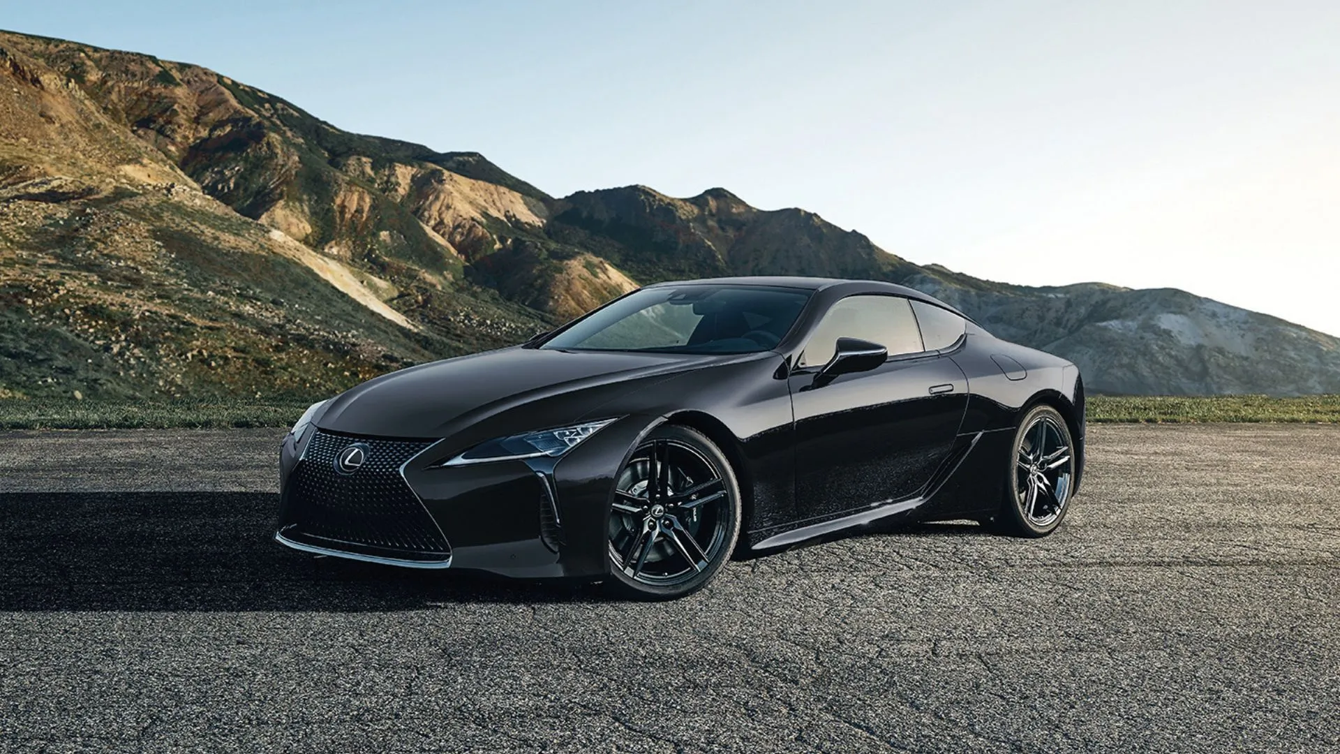 Lexus LC 2025 màu đen đỗ trên nền sỏi với phong cảnh núi hùng vĩ phía sau.