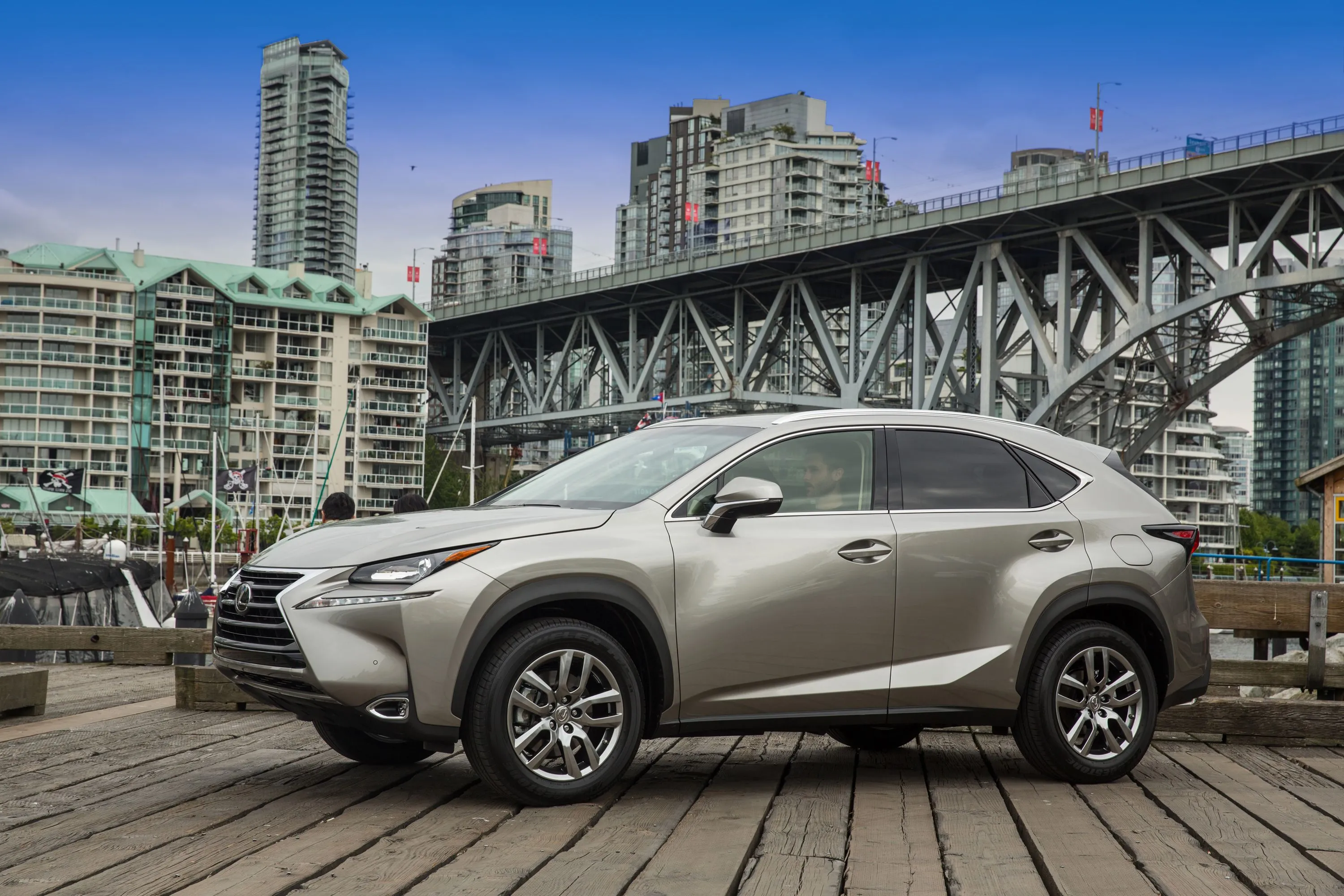 Lexus NX 200t 2017 màu xám đỗ nghiêng trước cây cầu, mẫu SUV crossover hạng sang với thiết kế thể thao và độ bền cao.