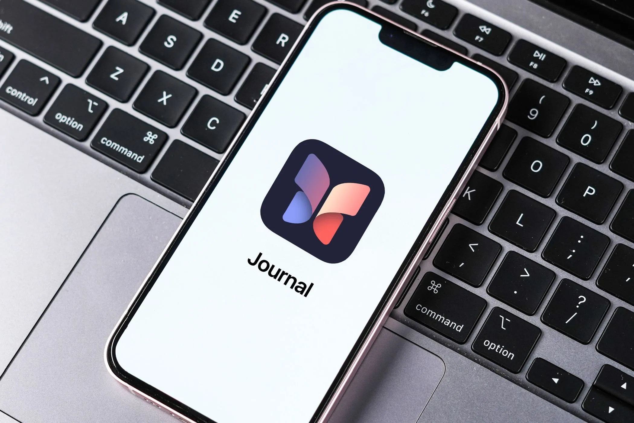 Màn hình iPhone hiển thị ứng dụng Journal của Apple đặt trên bàn phím MacBook, tượng trưng cho việc chuyển đổi từ nhật ký số sang giấy.