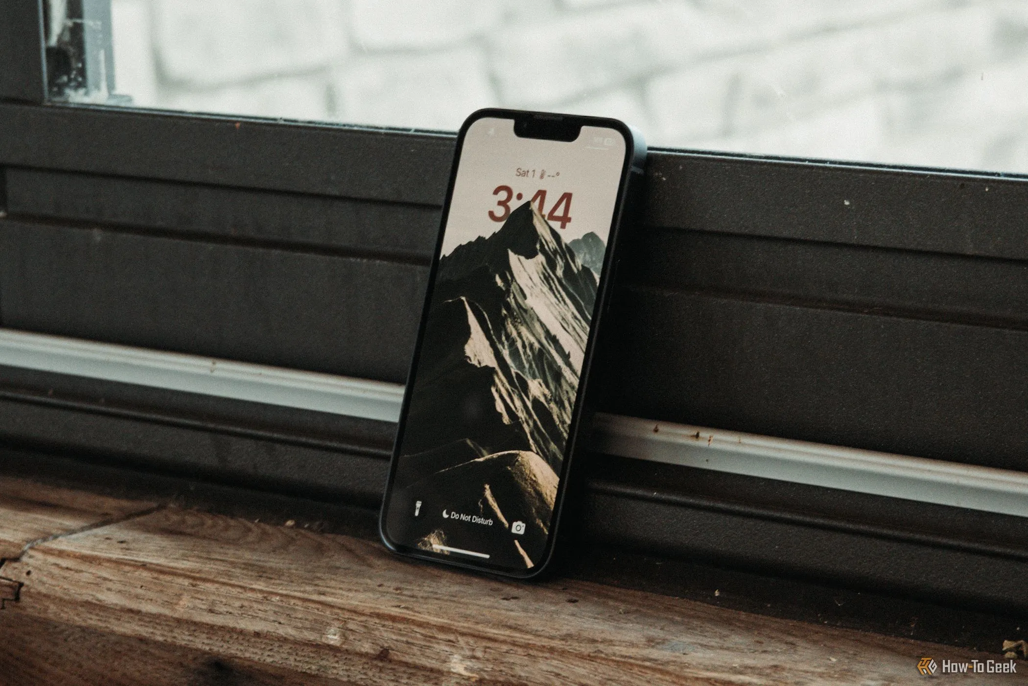 Màn hình khóa iPhone 16e hiển thị thời gian và thông báo, tựa vào cửa sổ.