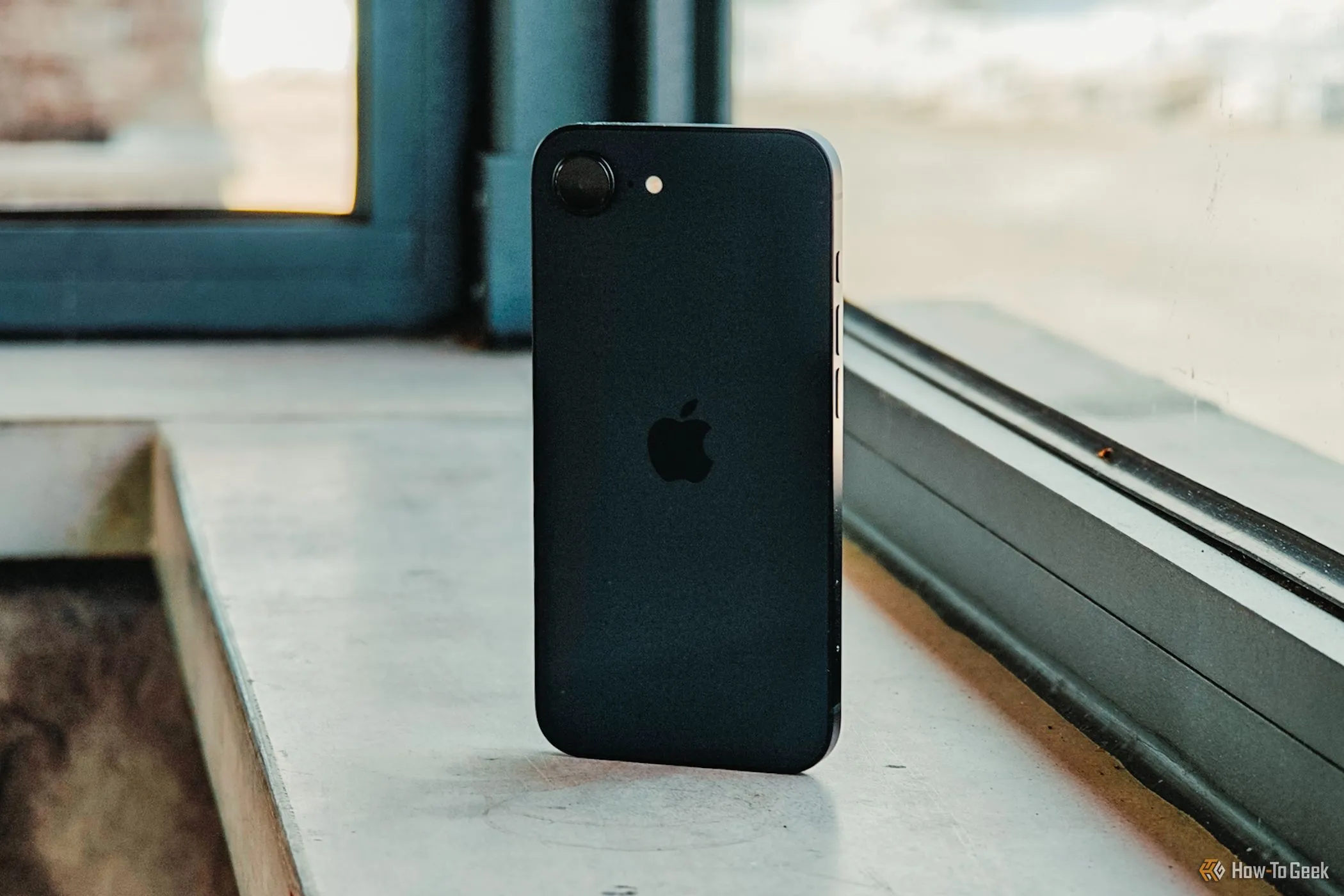 Mặt lưng iPhone 16e màu trắng đặt nghiêng trước cửa sổ