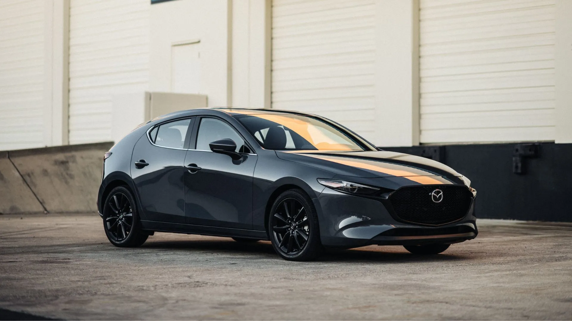 Mazda 3 Hatchback 2025 màu đen đỗ bên ngoài nhà kho, với thiết kế thể thao và cabin cao cấp, đây là lựa chọn hấp dẫn cho xe compact số sàn.