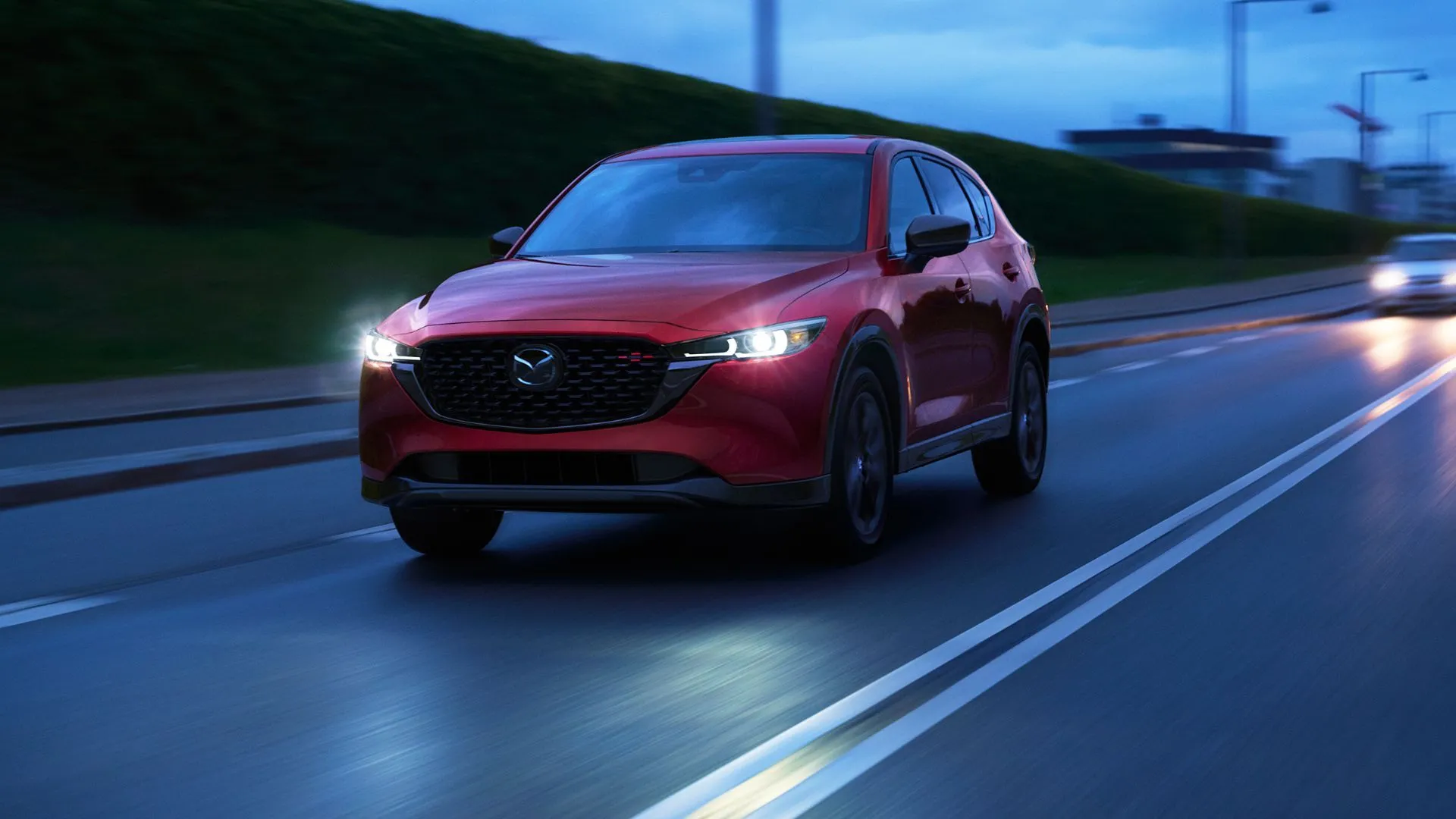 Mazda CX-5 2025 màu đỏ đô nổi bật đang di chuyển trong đô thị vào buổi tối.