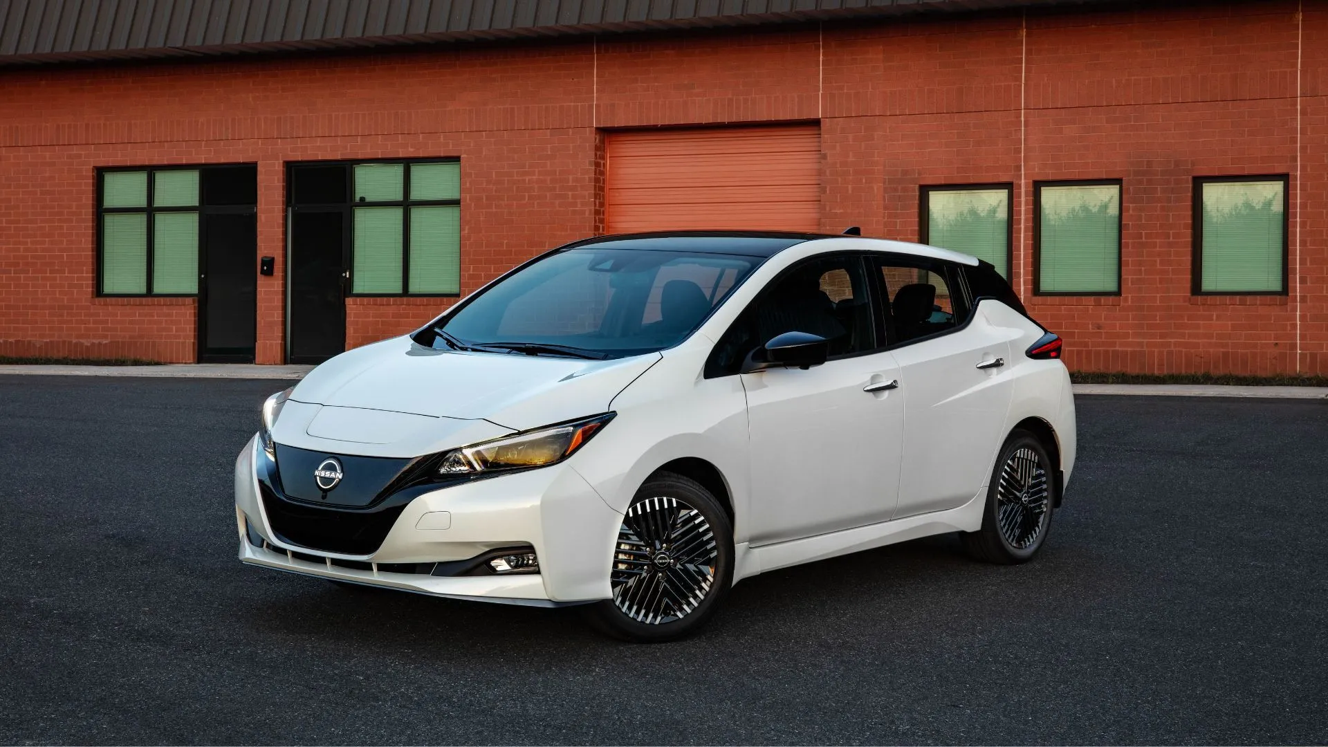 Nissan Leaf 2025 màu trắng đỗ trước tòa nhà gạch, mẫu xe điện đô thị